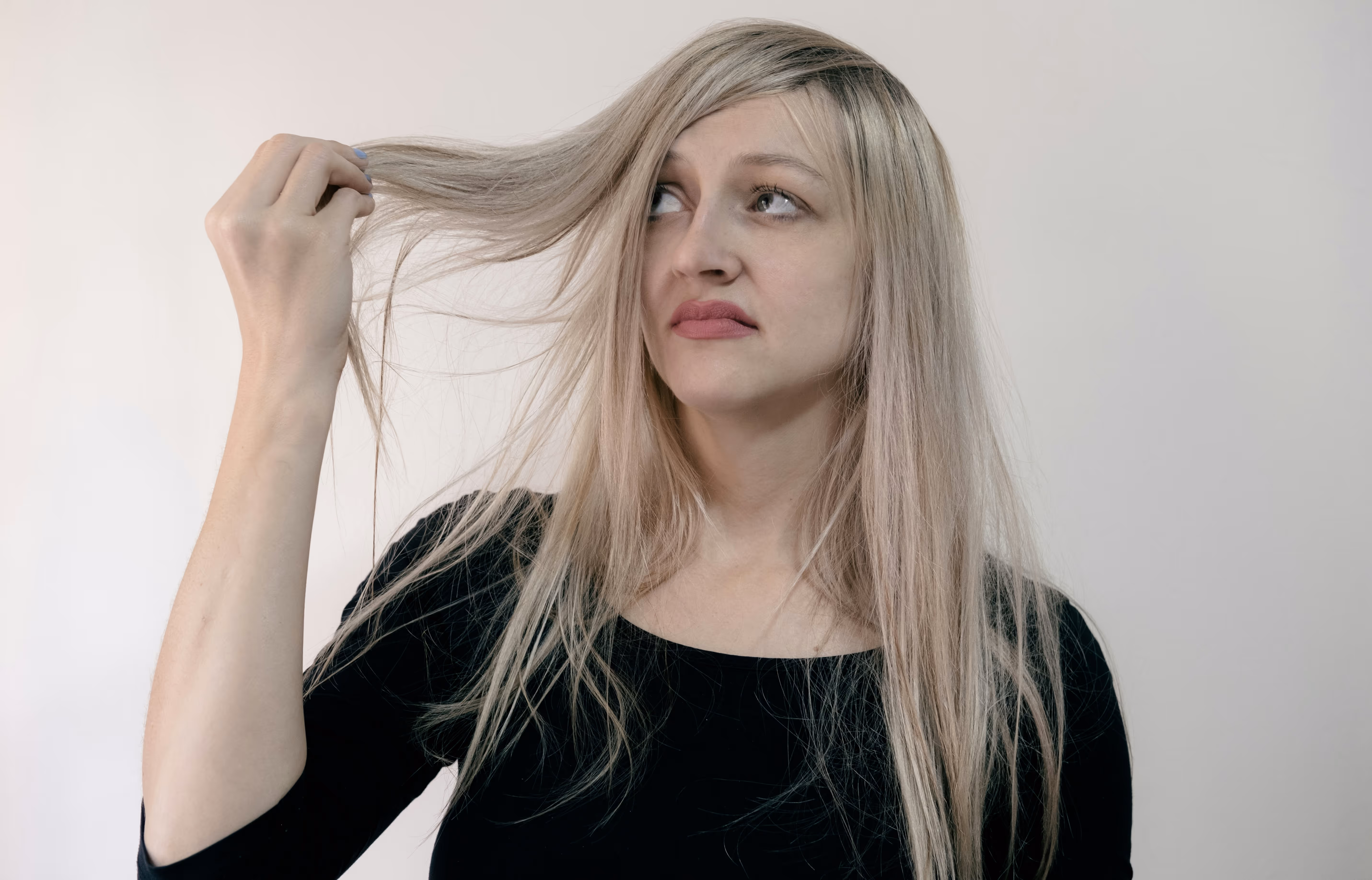 Femme aux cheveux blonds touchant ses mèches, expression soucieuse. Représentation des cheveux affaiblis liés à l'alopécie.