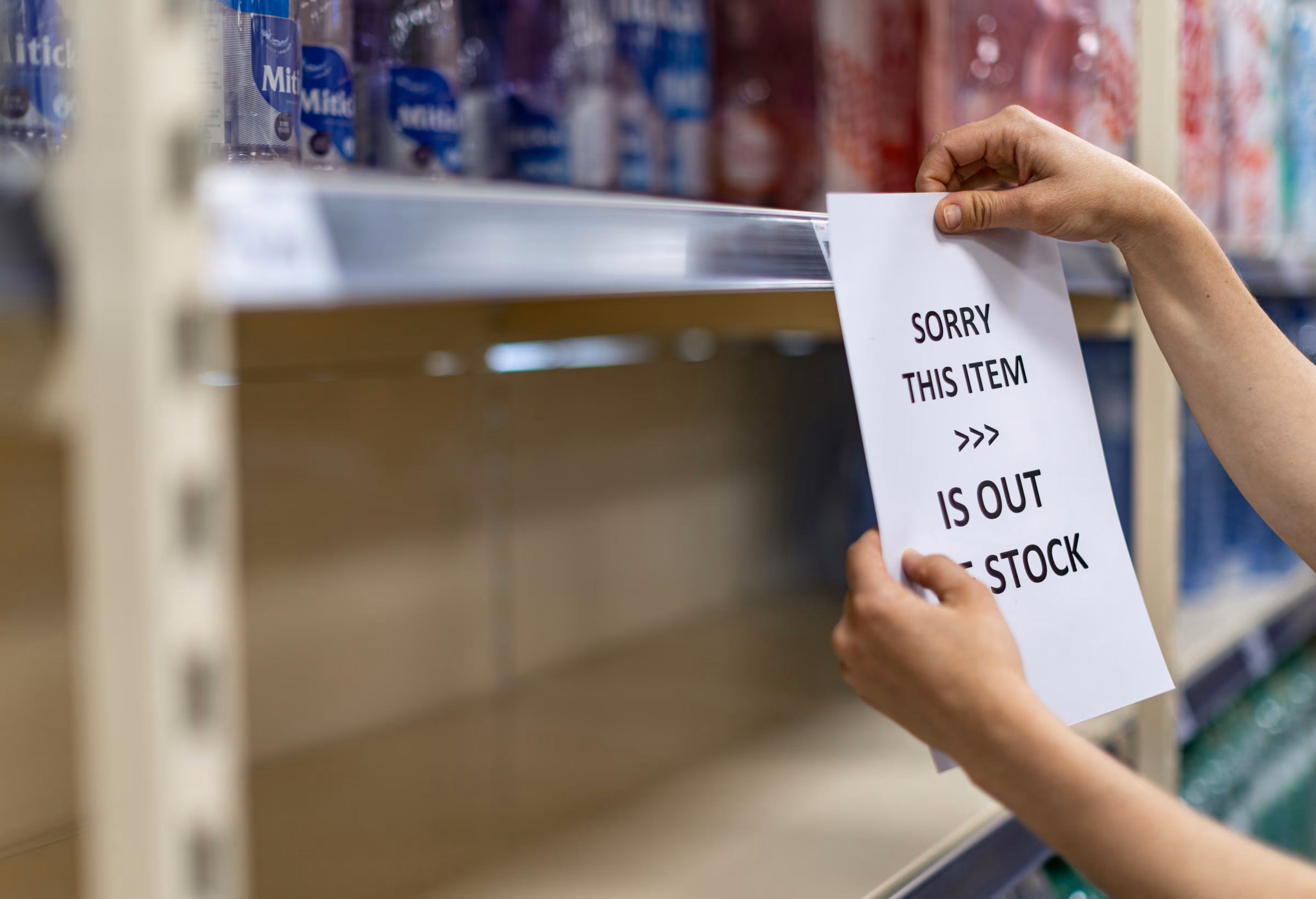 Main plaçant un panneau rupture de stock sur une étagère vide. Indisponibilité produit, gestion des stocks et approvisionnement en magasin.