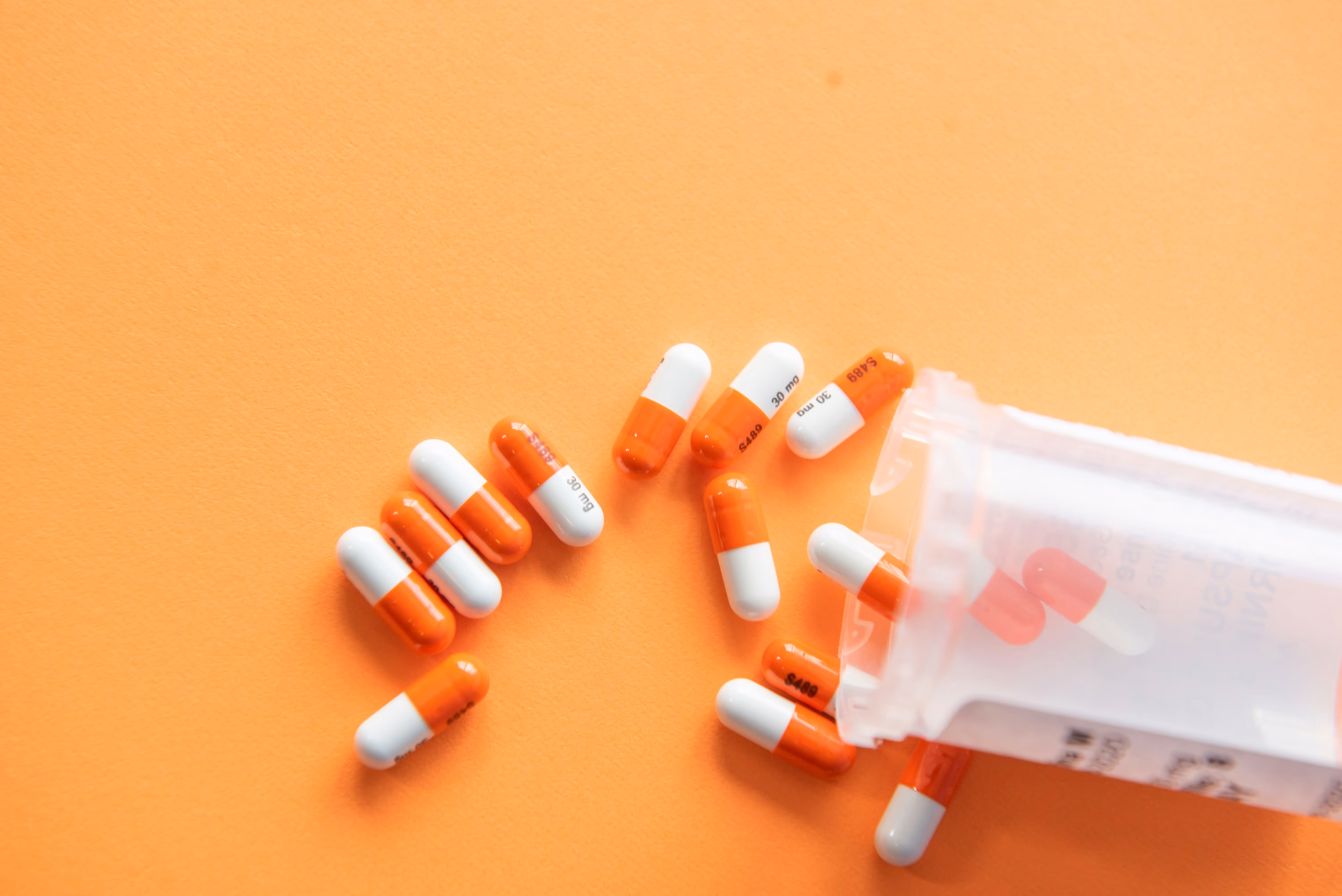 Gélules de traitement pour la chute de cheveux s'échappant d'un flacon orange.