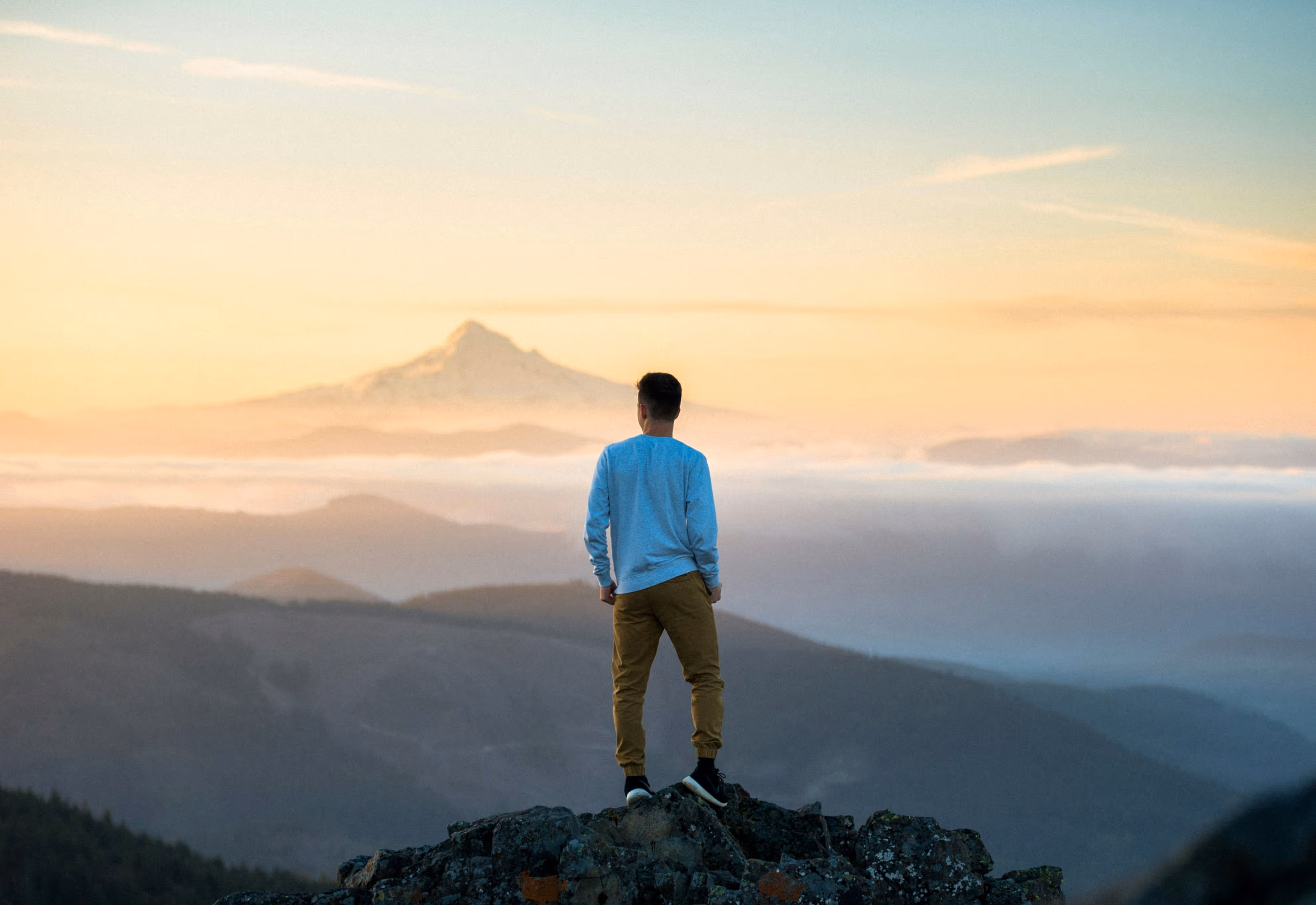 Un homme de dos regarde un paysage de montagne brumeux au lever du soleil. Représentation métaphorique de l'espoir.