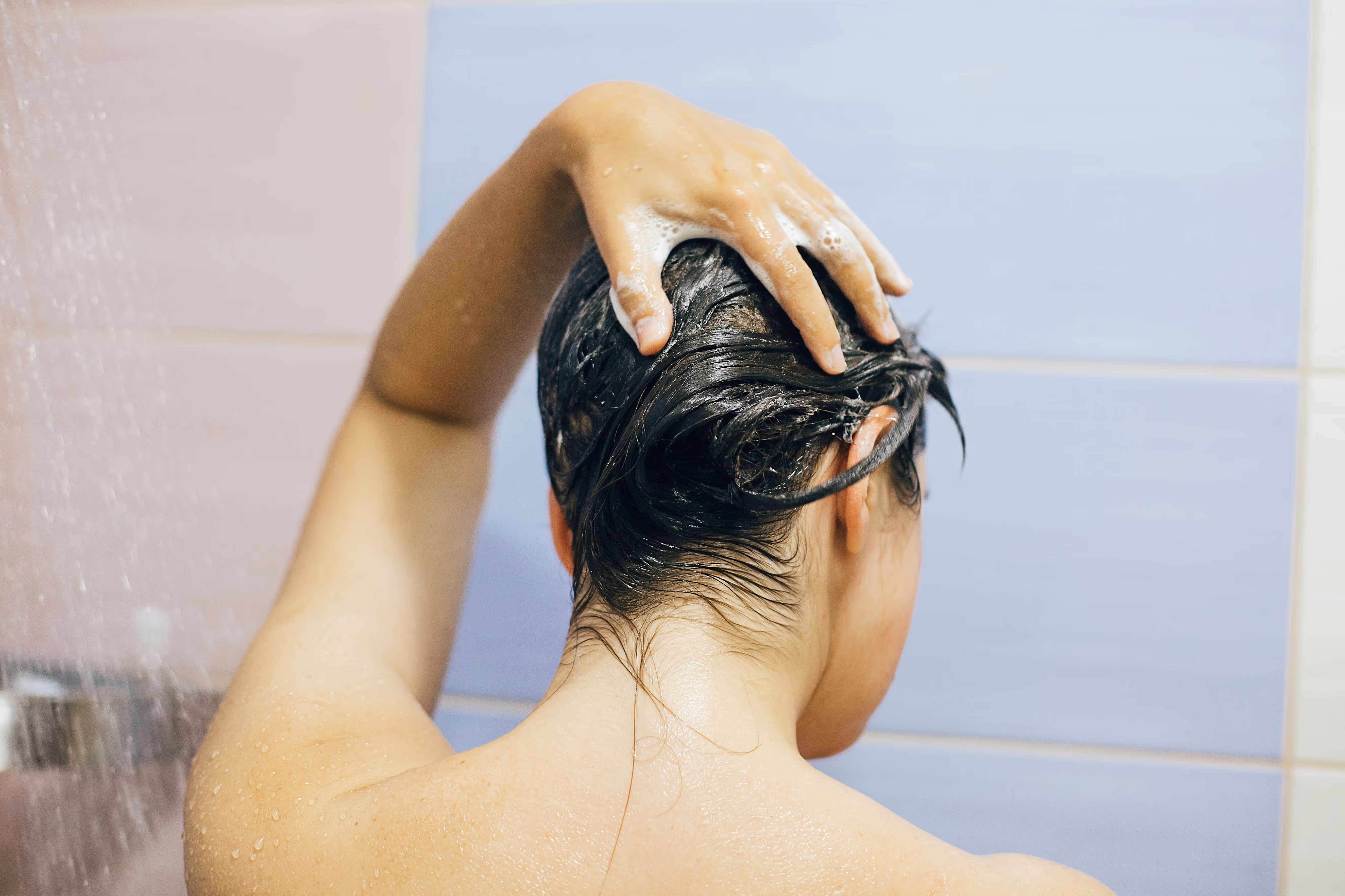 Personne se lavant les cheveux sous la douche, vue de dos.