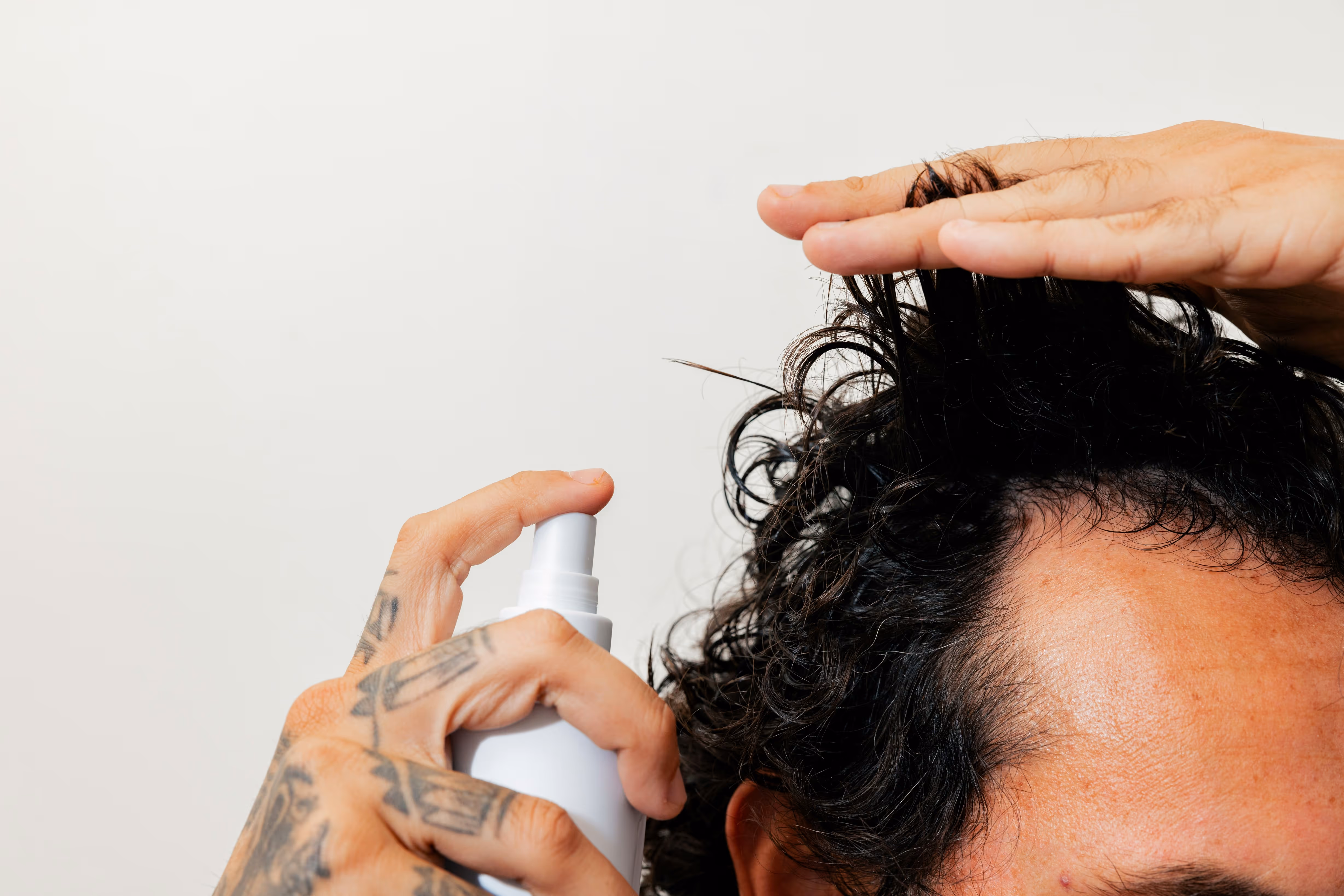 Application d'un spray capillaire sur cuir chevelu d'homme pour le soin des cheveux bouclés et contre la perte de cheveux.