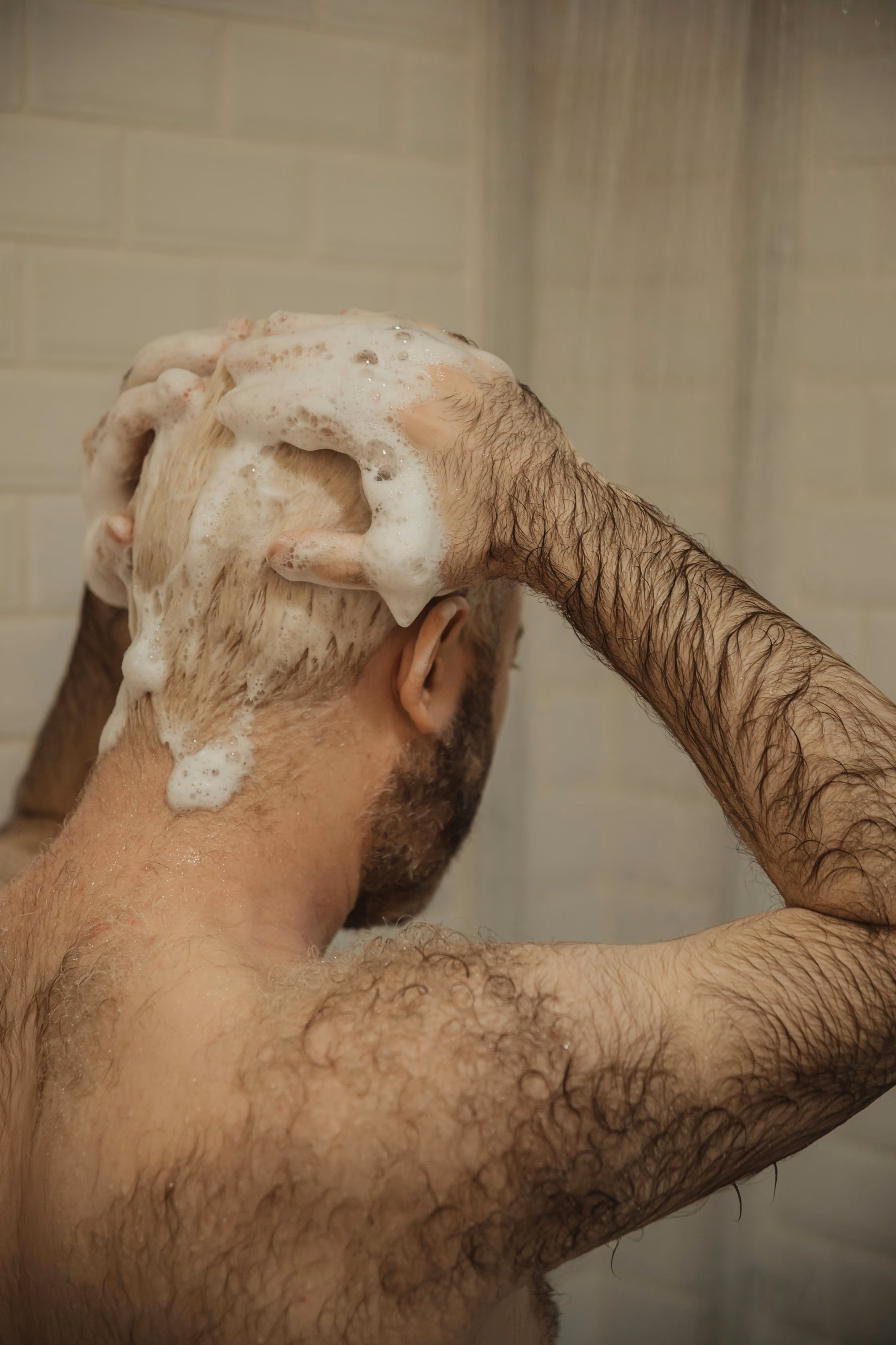 Homme barbu et velu se lavant les cheveux blonds décolorés sous la douche avec de la mousse.