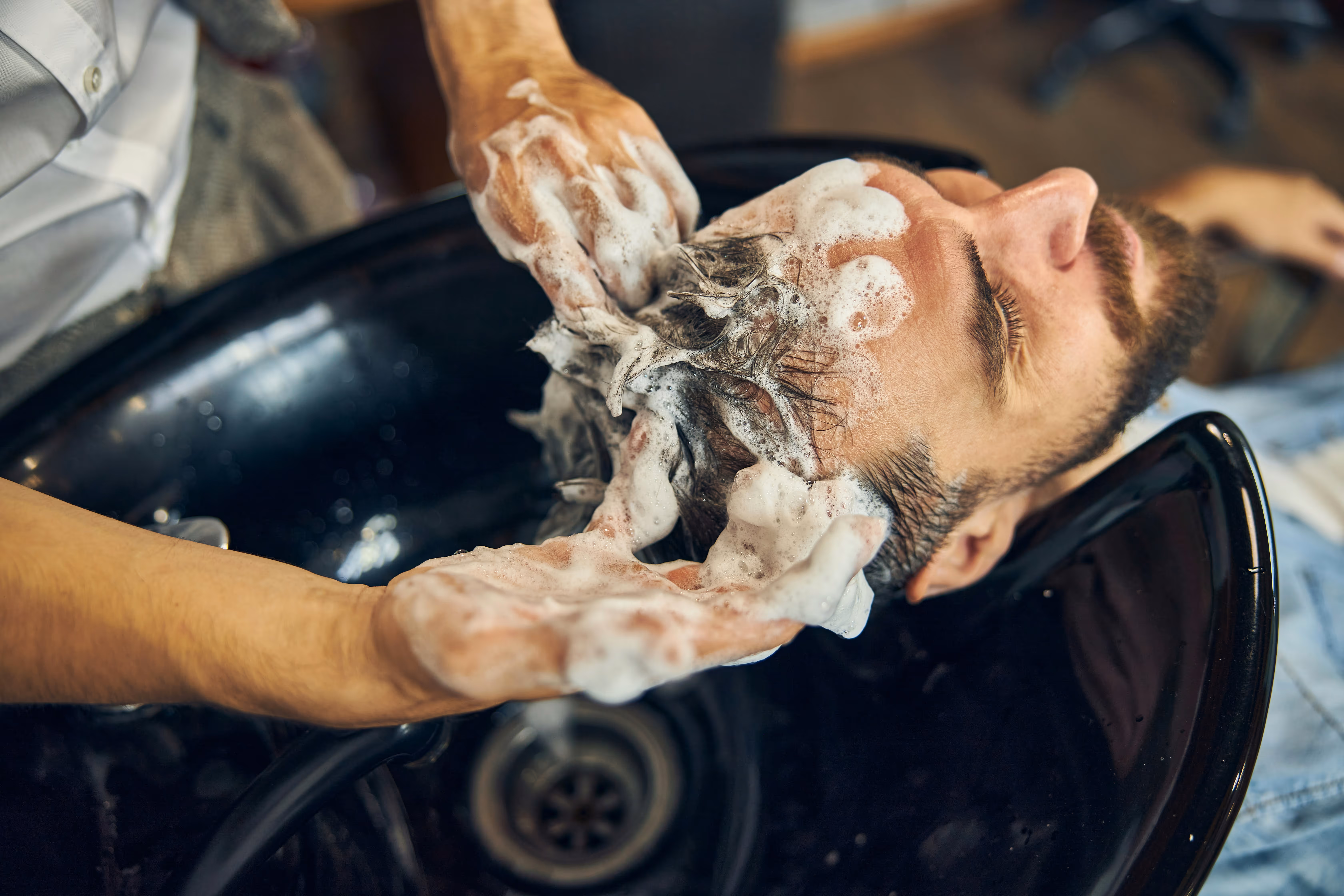 Homme se faisant laver les cheveux par un coiffeur avec du shampooing au bac.