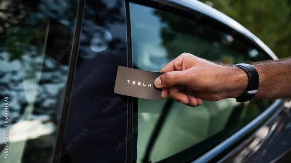 Schlüsselkarte von Tesla von einer Hand an die Autoscheibe gehalten