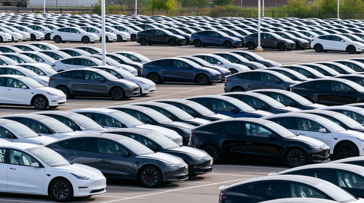 Zahlreiche Tesla Model 3 und Model Y stehen in langen Reihen auf einem Fahrzeugplatz. (KI-generiert)
