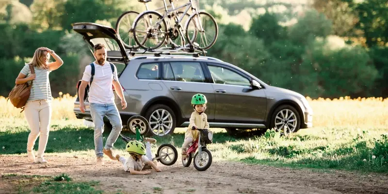 Glückliche Familie mit E-Auto und Fahrrädern