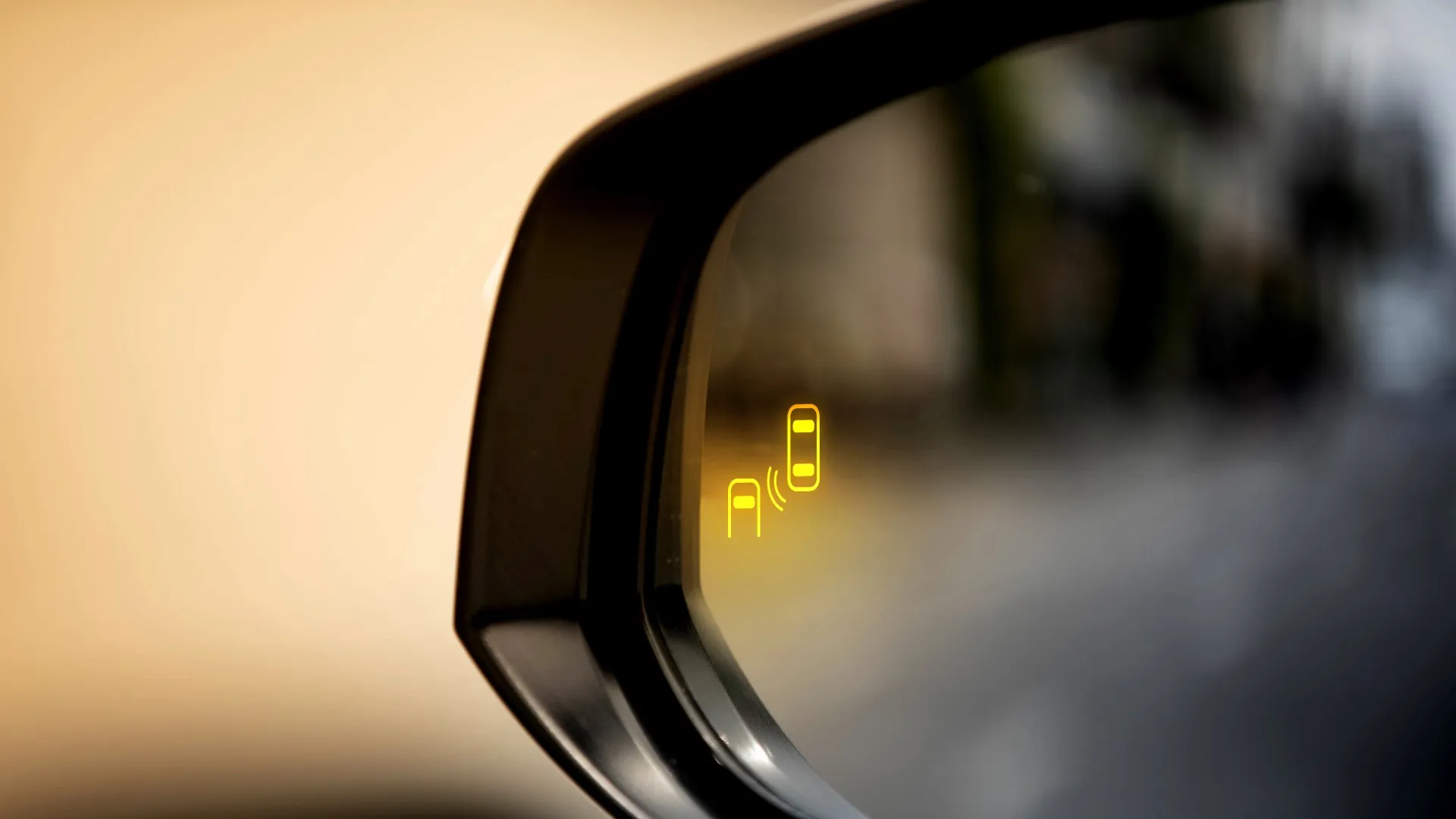Car side mirror with illuminated yellow blind spot warning indicator showing two cars.
