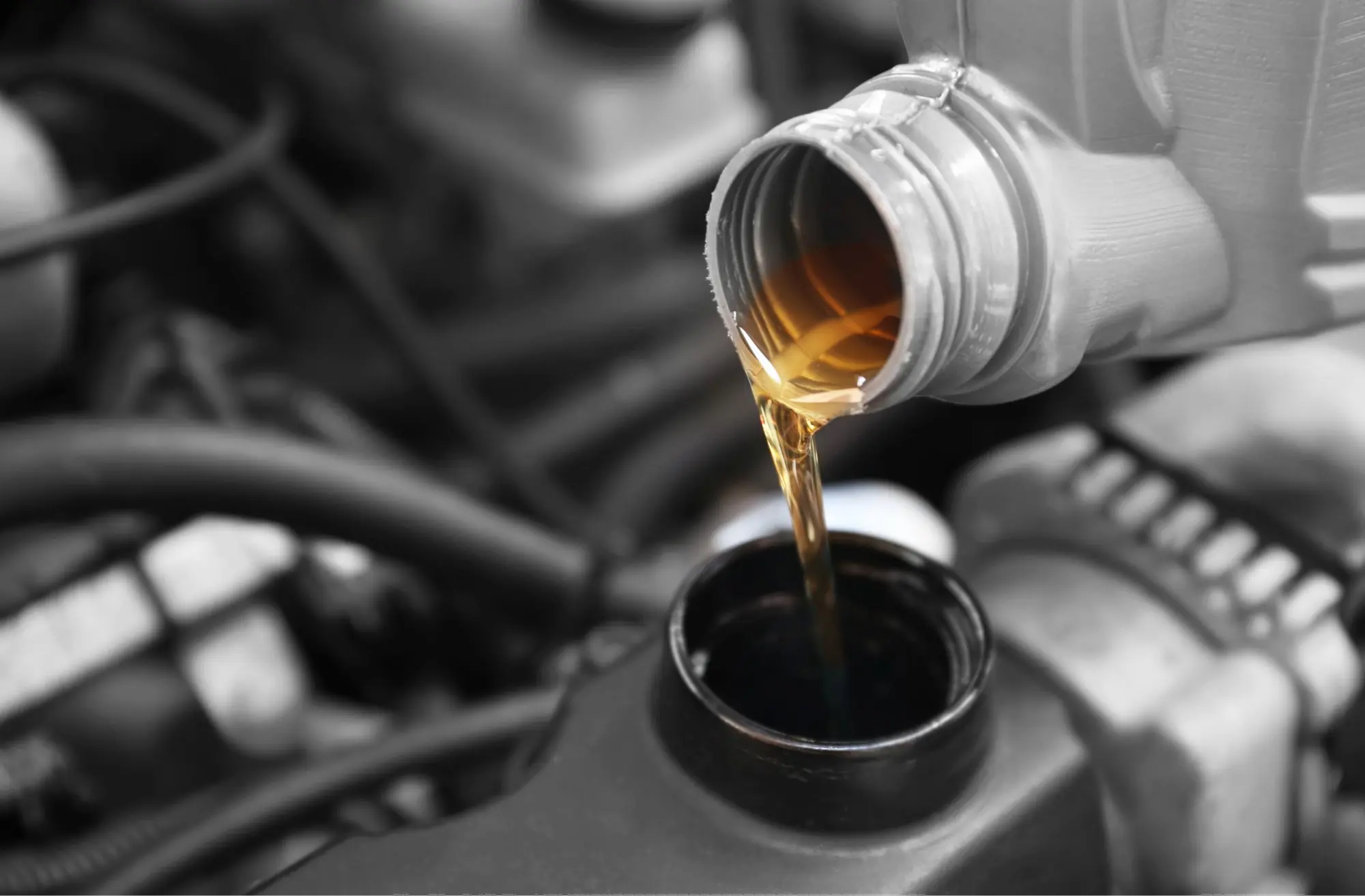 Golden engine oil pouring from a plastic container into a car engine reservoir.