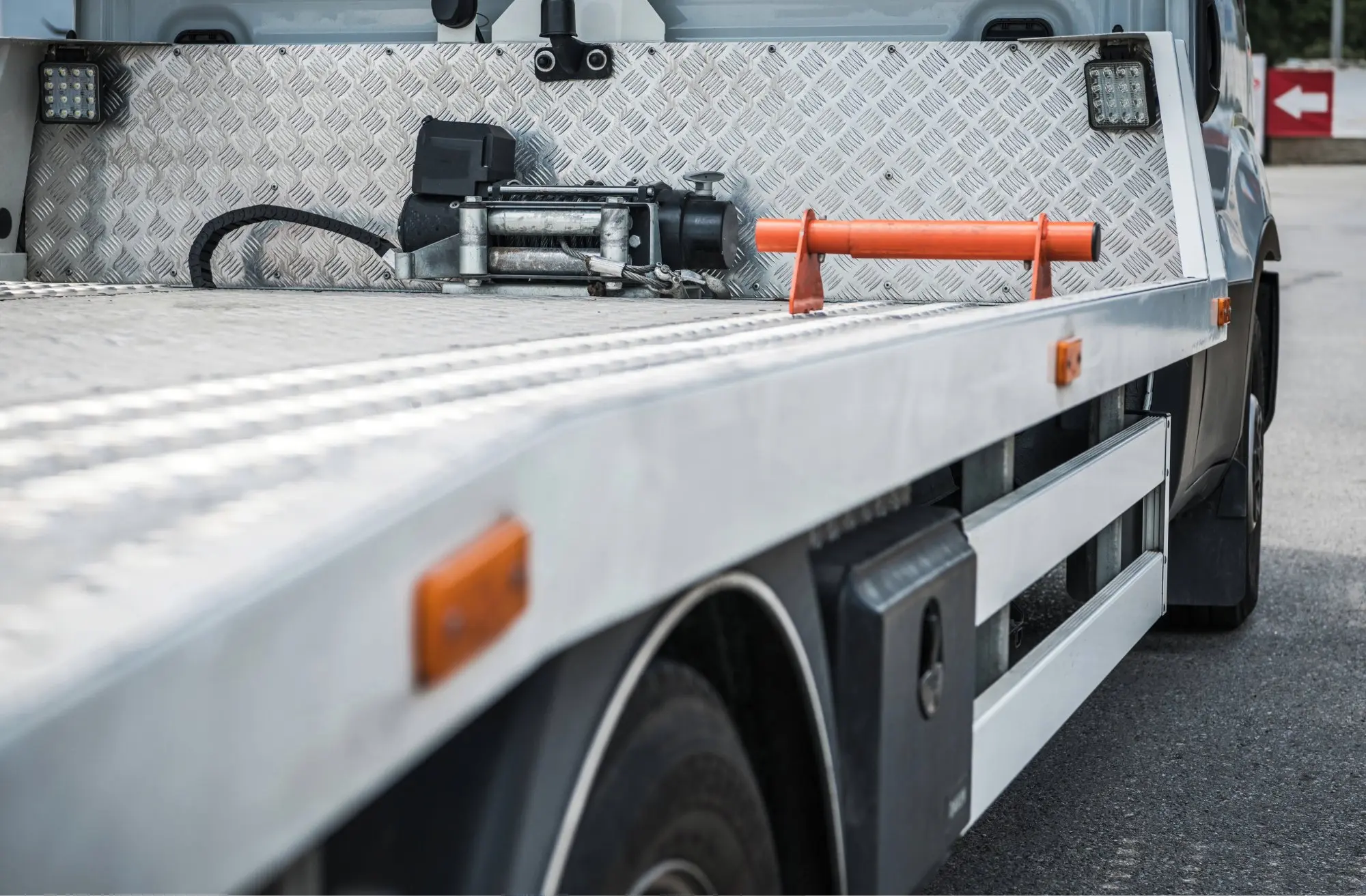 Side view of flatbed tow truck with metal winch and orange handle on bed surface.
