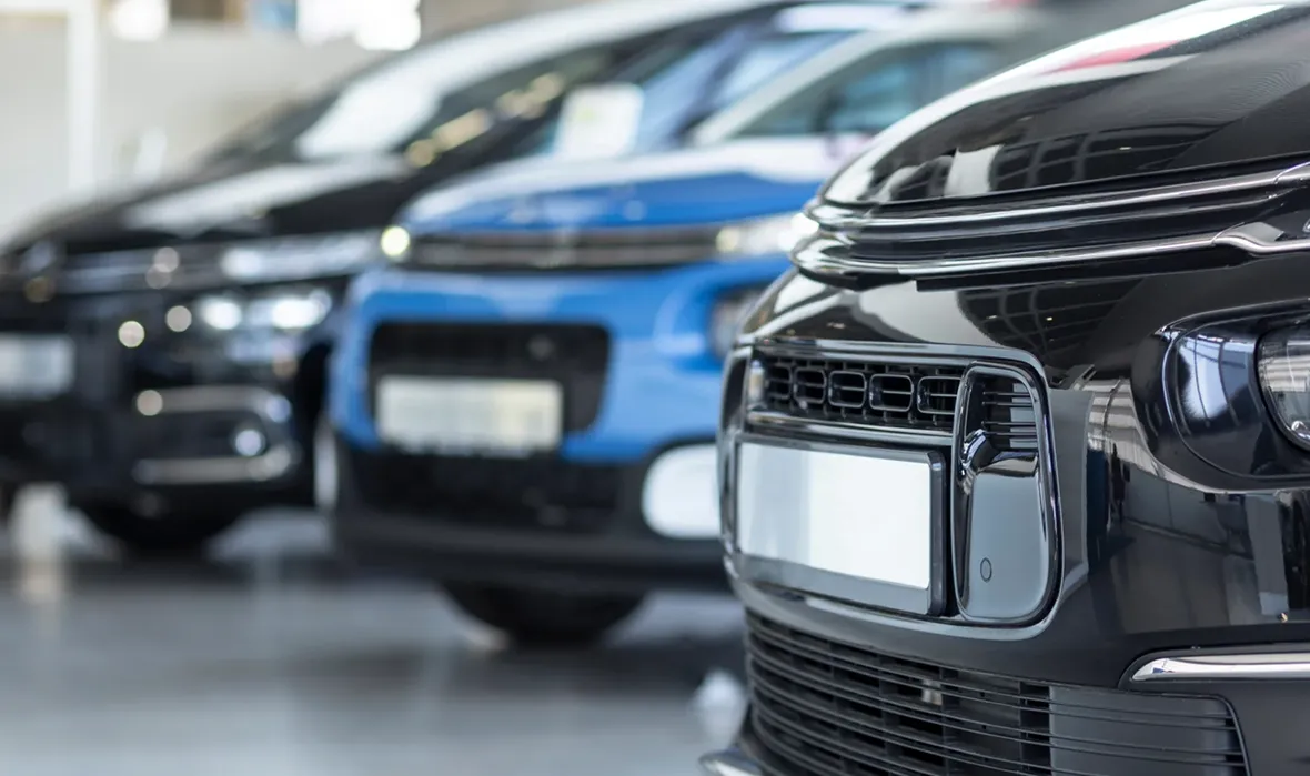 A row of new cars parked inside a dealership showroom, featuring a black car in sharp focus upfront