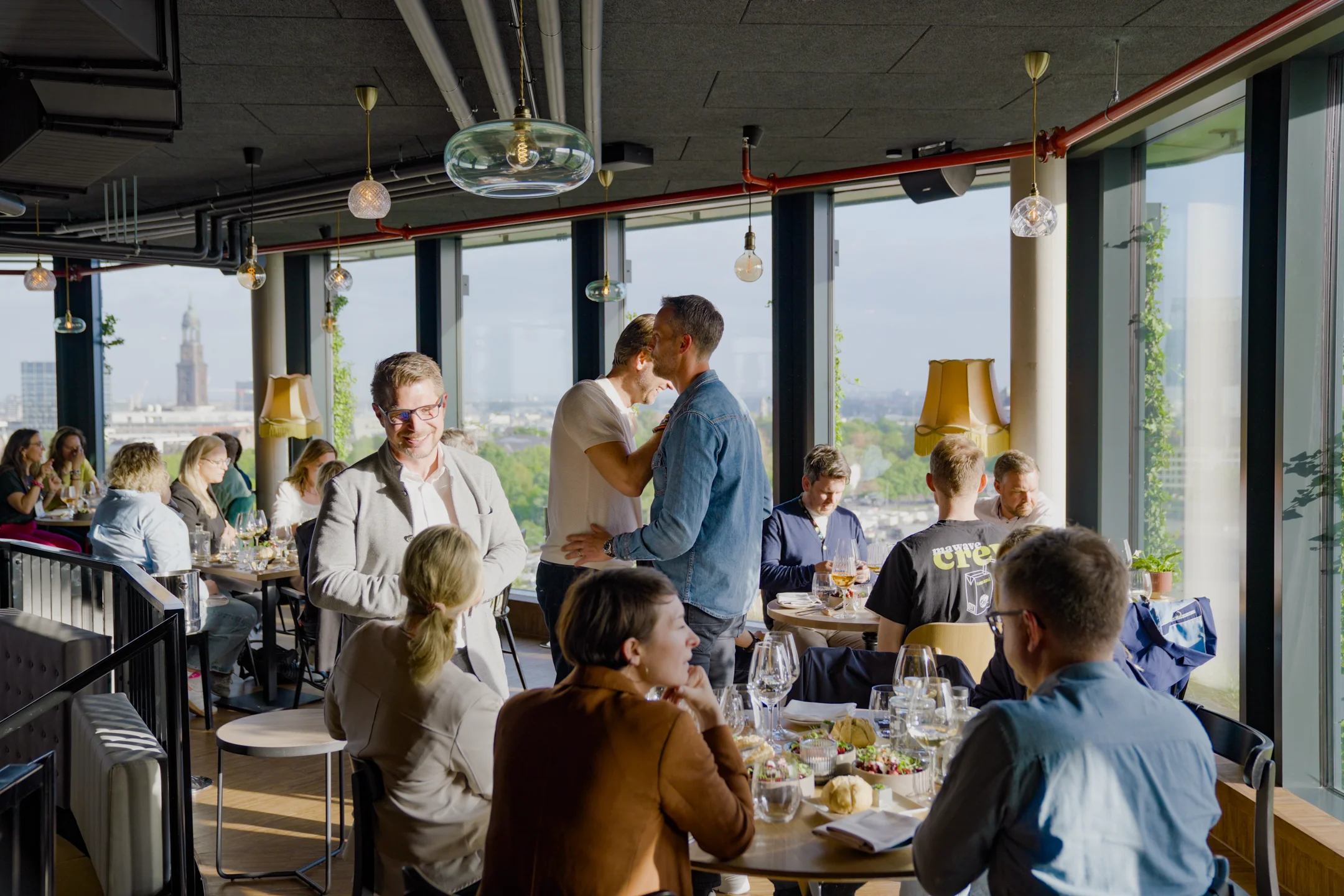 Menschen unterhalten sich und essen in einem modernen Restaurant mit großen Fenstern und Stadtblick.