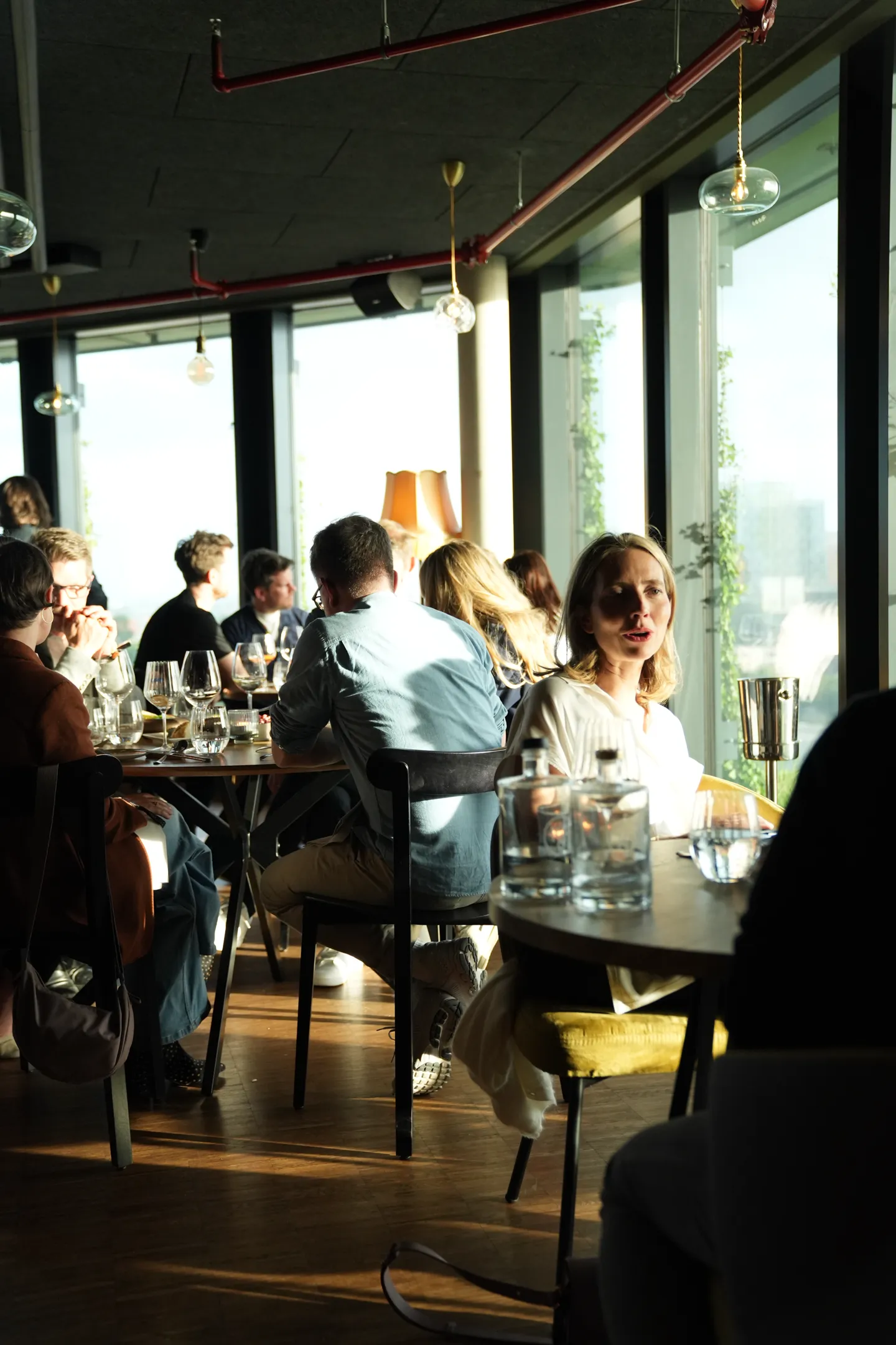 Menschen sitzen in einem hellen Restaurant mit großen Fenstern und unterhalten sich bei Sonnenlicht.