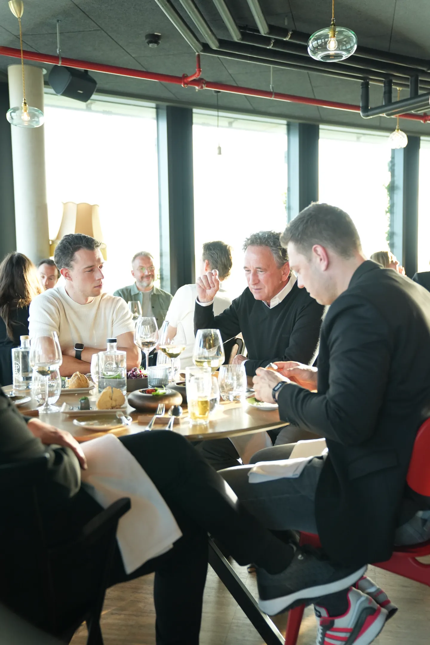 Menschen sitzen in einem modernen Restaurant um einen Tisch mit Essen und Getränken, im Gespräch und entspanntem Ambiente.
