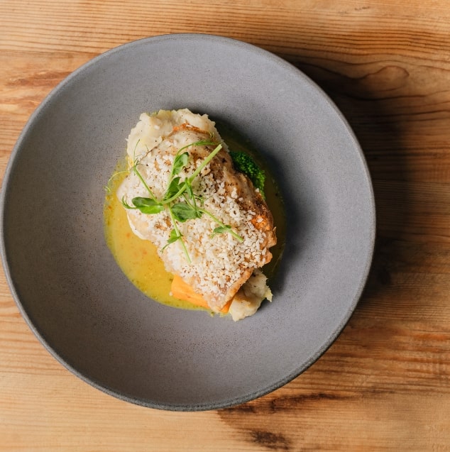 fish on top of a bed of sauce plated on a table