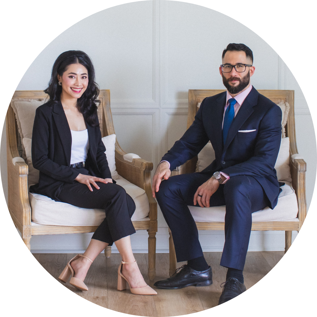A woman and a man dressed in business attire sitting on wooden armchairs against a white paneled wall.