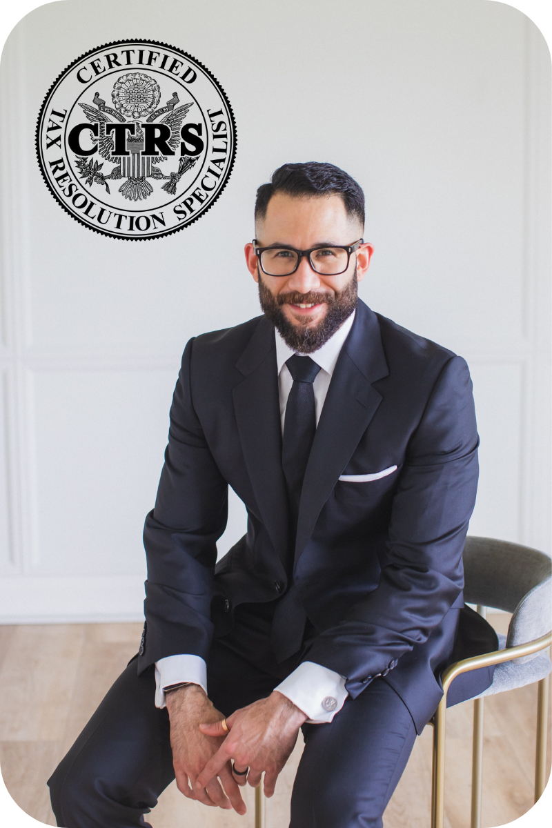 Bearded man with glasses wearing a black suit and tie, sitting on a chair and smiling, with a Certified Tax Resolution Specialist logo in the background.