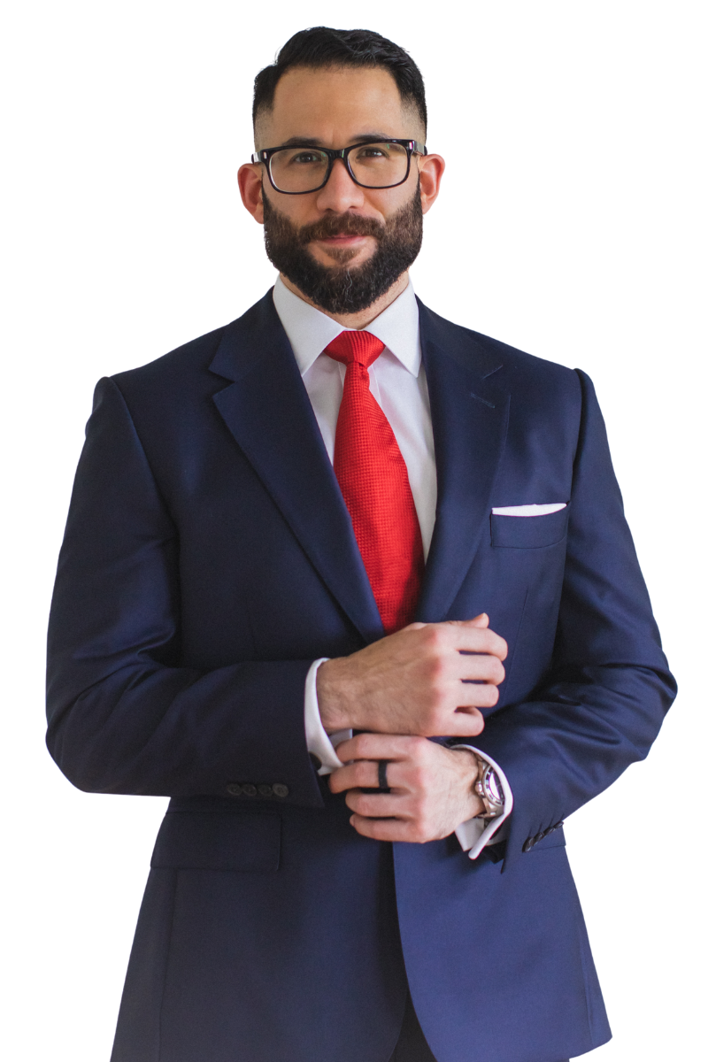 Man with beard and glasses adjusting his cuff wearing a navy blue suit, white shirt, and red tie.