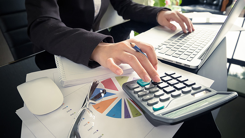 Business woman using a calculator to calculate the numbers on his desk in a office.