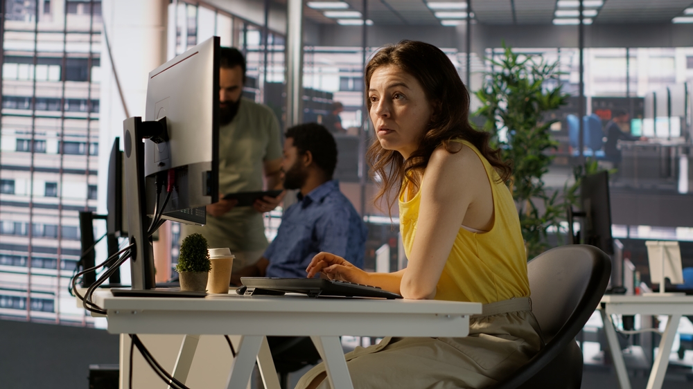 Worker sitting at office desk using computer during job shift, looking through online financial business documents.
