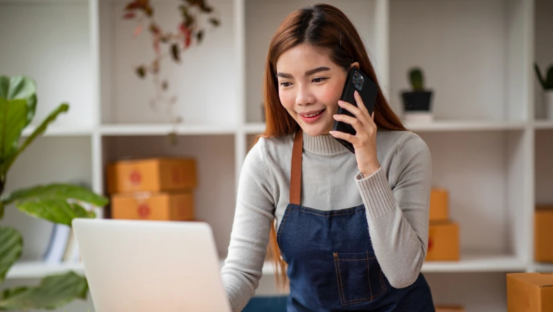 Stylish small business owner Young Asian woman using laptop computer in her home office, small business entrepreneur SME, working with a box at home, Online selling, e-commerce, packing concept.