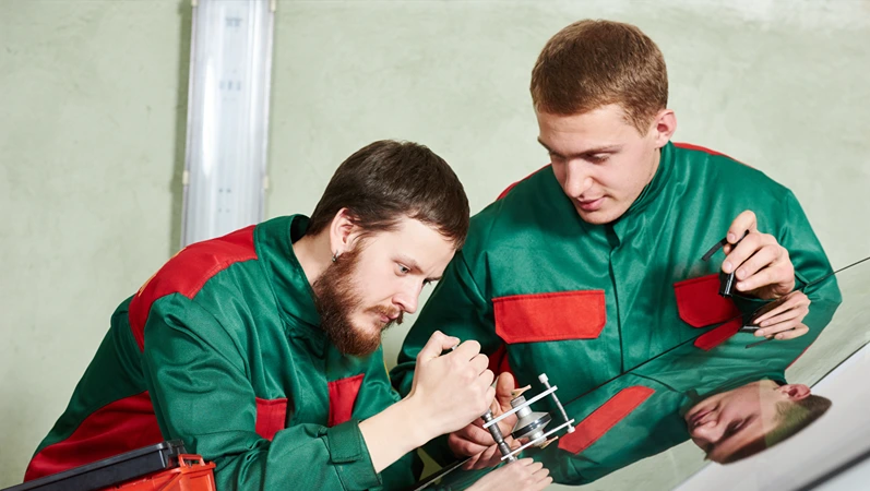 Automobile glazier repairman teaching or discussing with partner windscreen repair of a car in auto service station garage