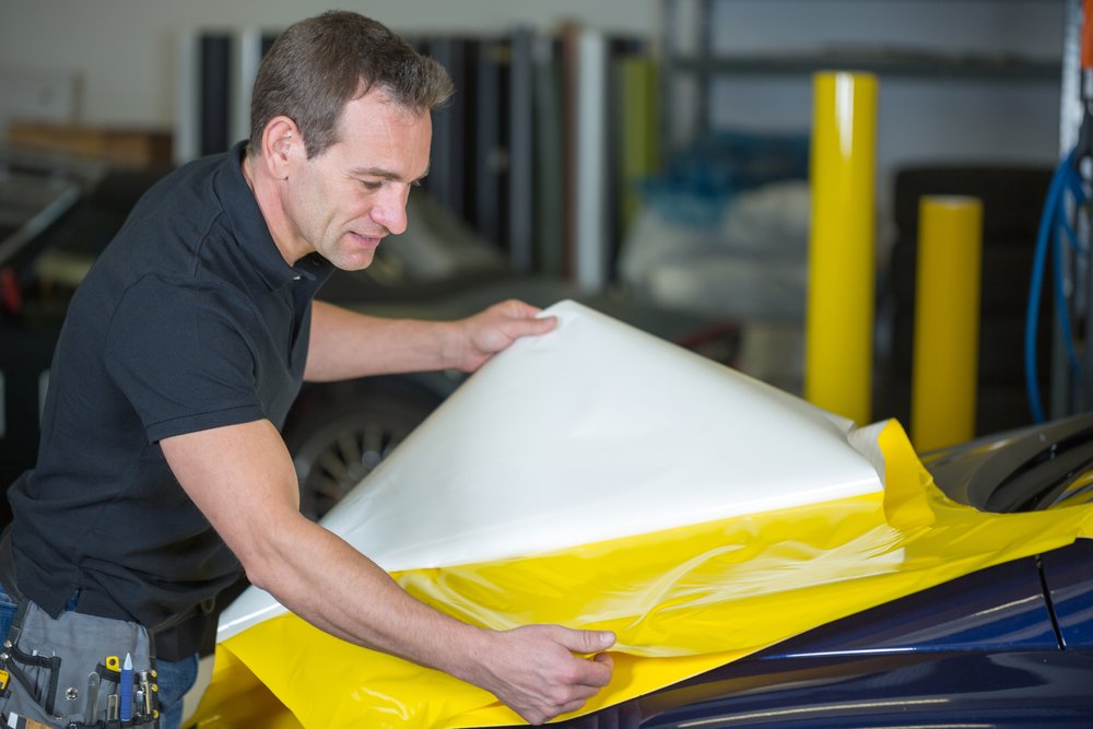 Car wrapper preparing yellow foil to wrap a vehicle