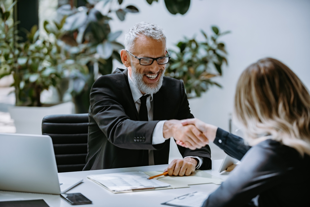Happy mature man in formalwear shaking hand to successful job candidate in the modern office