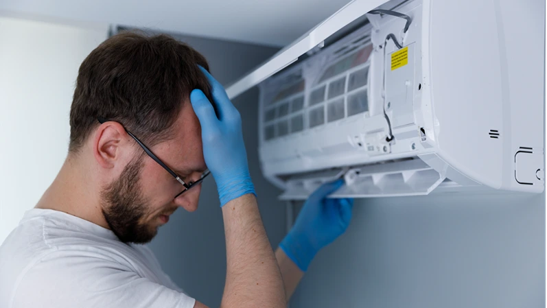 Frustrated technician dealing with air conditioning repair while wearing blue gloves, showing signs of stress and concentration in a modern residential environment