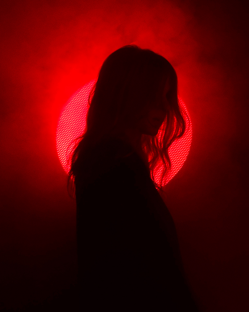 Silhouette of a person standing before a glowing red circular light in a dramatic atmosphere.