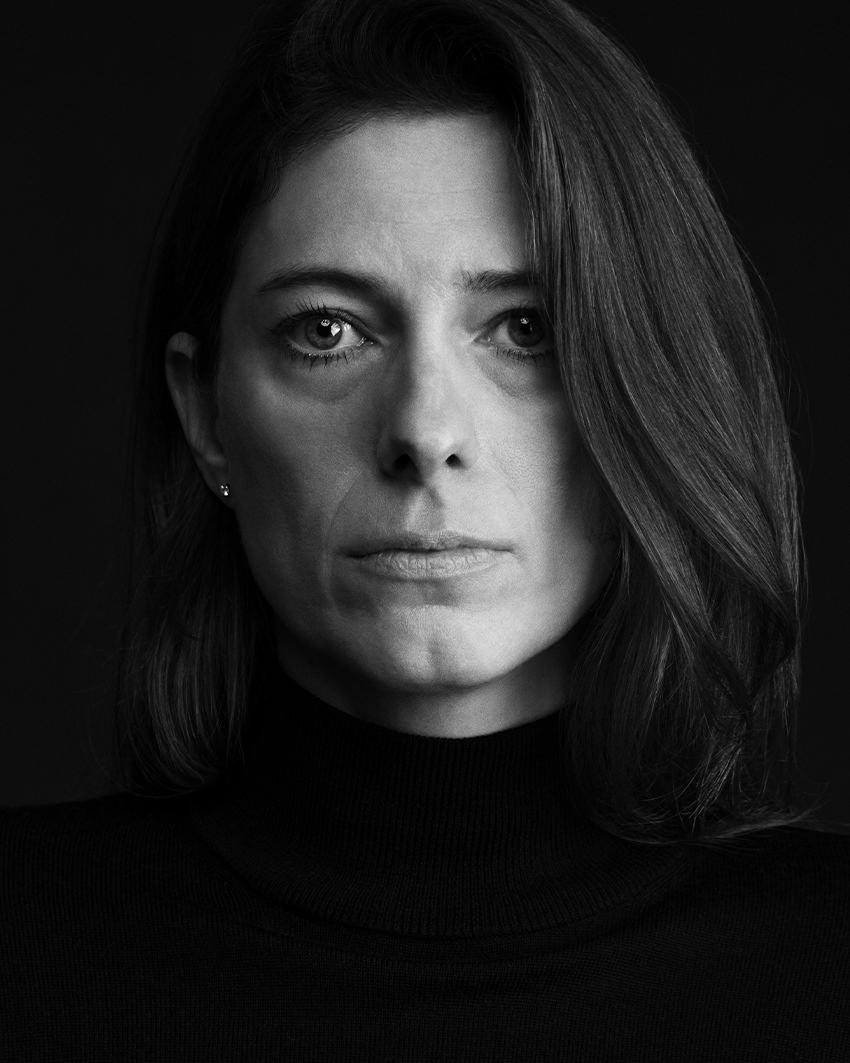 Black and white portrait of a woman in a dark turtleneck looking straight into the camera with a serious expression.
