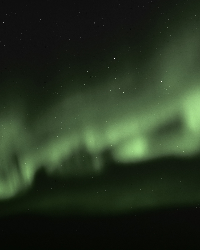 Green Northern Lights stretching across a star-filled night sky above a dark horizon.