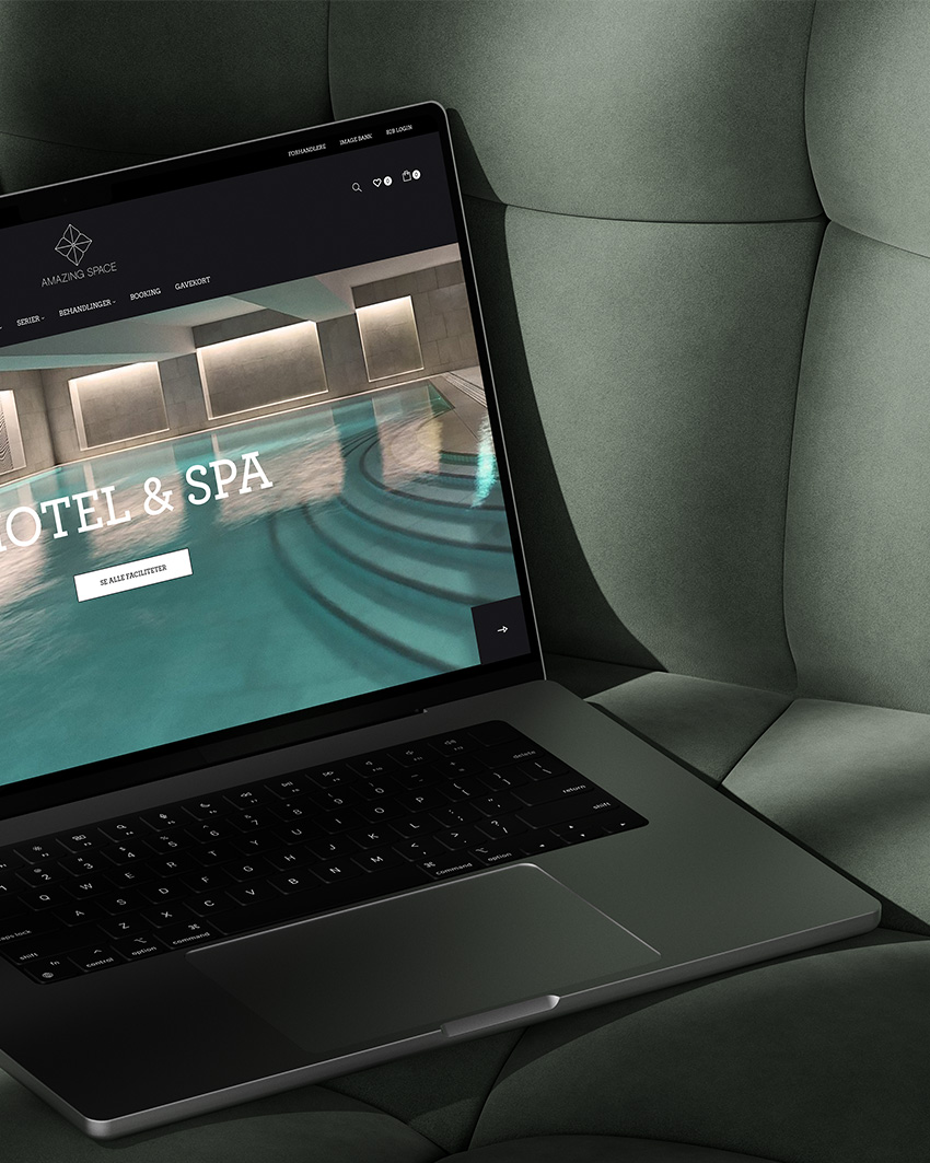 Close-up laptop mockup showcasing Amazing Space's website design with a modern indoor pool background, placed on a dark green cushioned surface.