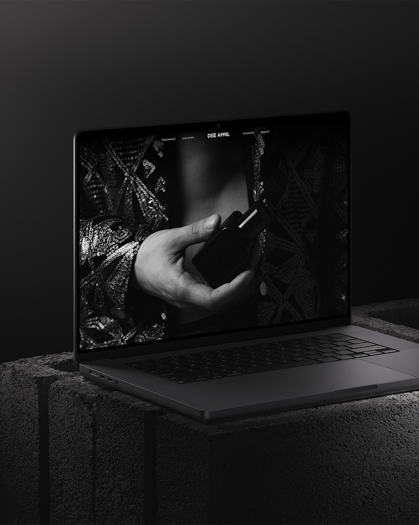 Laptop mockup displaying DEE APRIL’s black and white website design, featuring a close-up of a hand holding a perfume bottle.