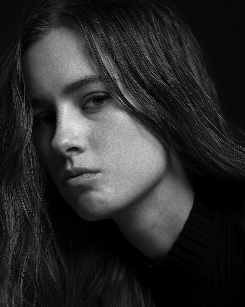 Black and white portrait of Maria-May Backhaus Brown with long hair and a dark sweater, captured in a dramatic close-up with soft lighting.