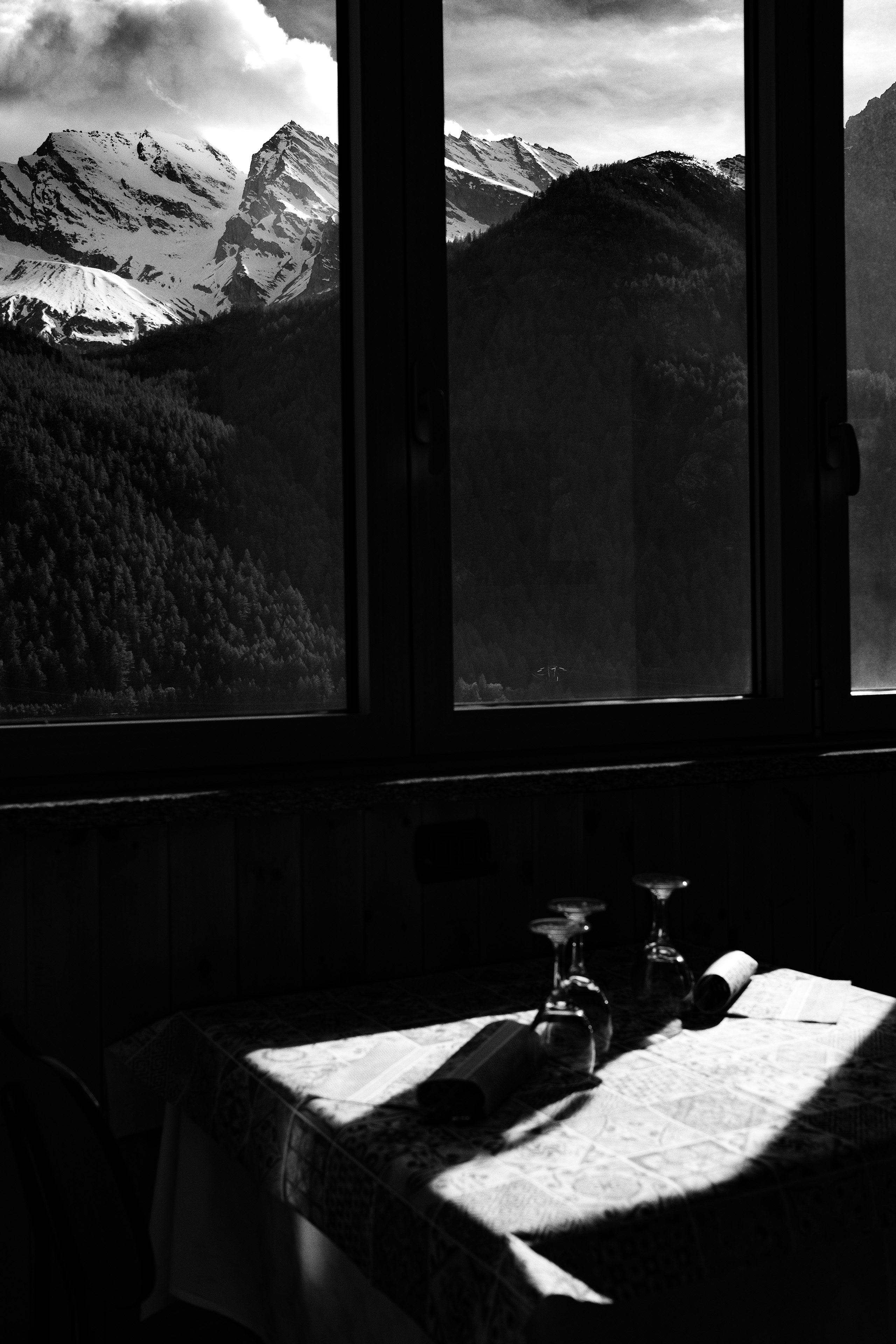 Black and white view through a window overlooking an alpine lake and snow-covered mountains in Gran Paradiso, Italy.