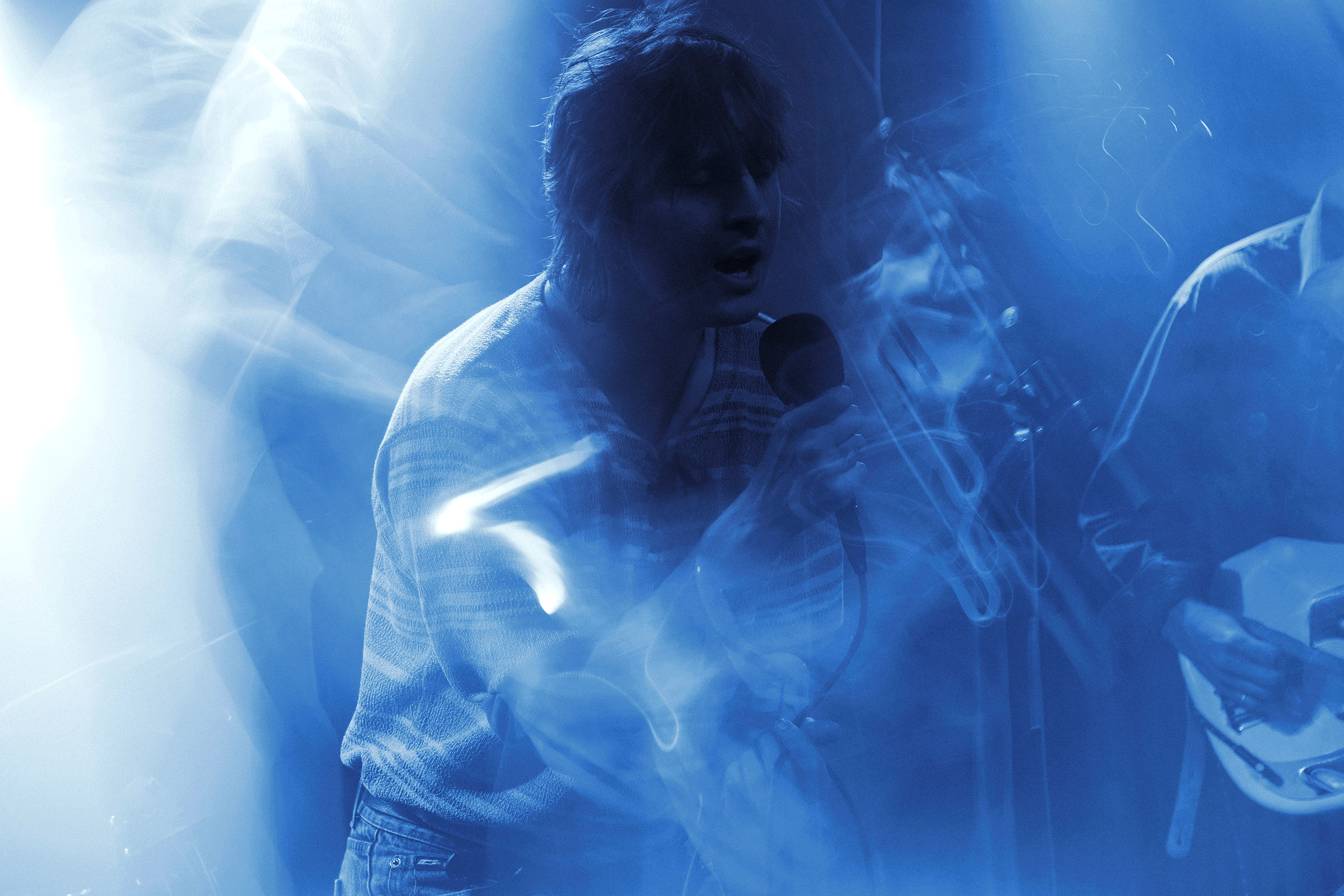 Thoughtfool performing with acoustic guitar at Rust in Copenhagen surrounded by blue stage lights and smoke.
