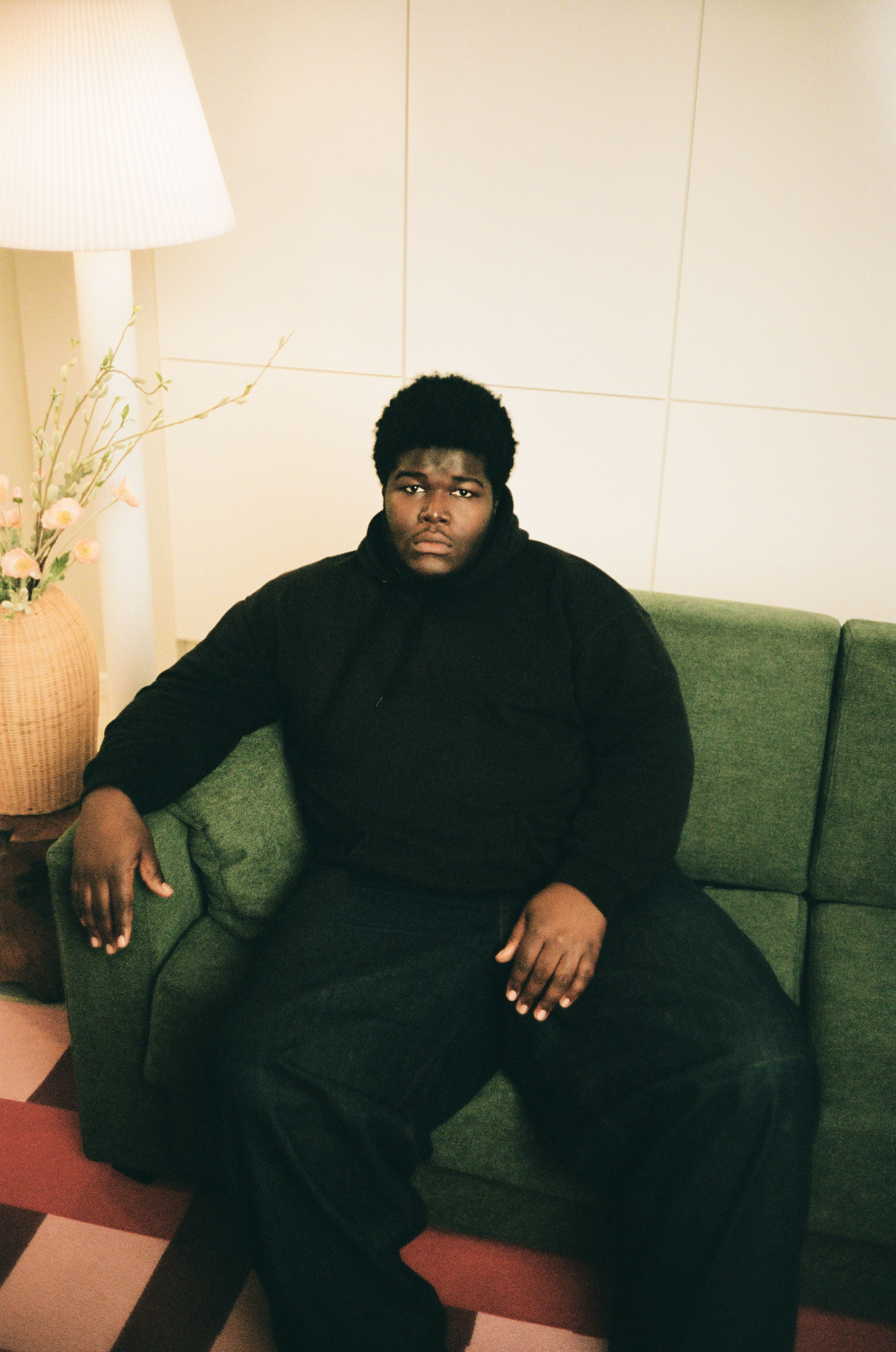 Lifestyle portrait of Danish artist BUKURU sitting on a green sofa in a warm-toned interior.