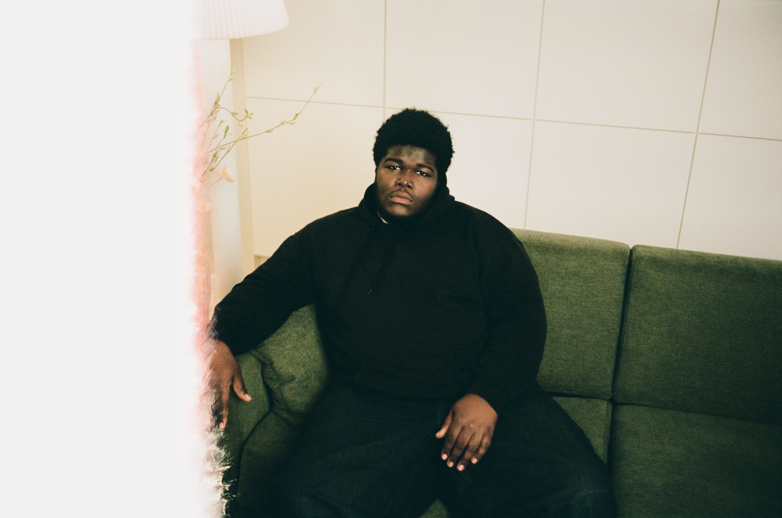 Editorial portrait of Danish artist BUKURU seated on a green sofa in a minimalist interior.