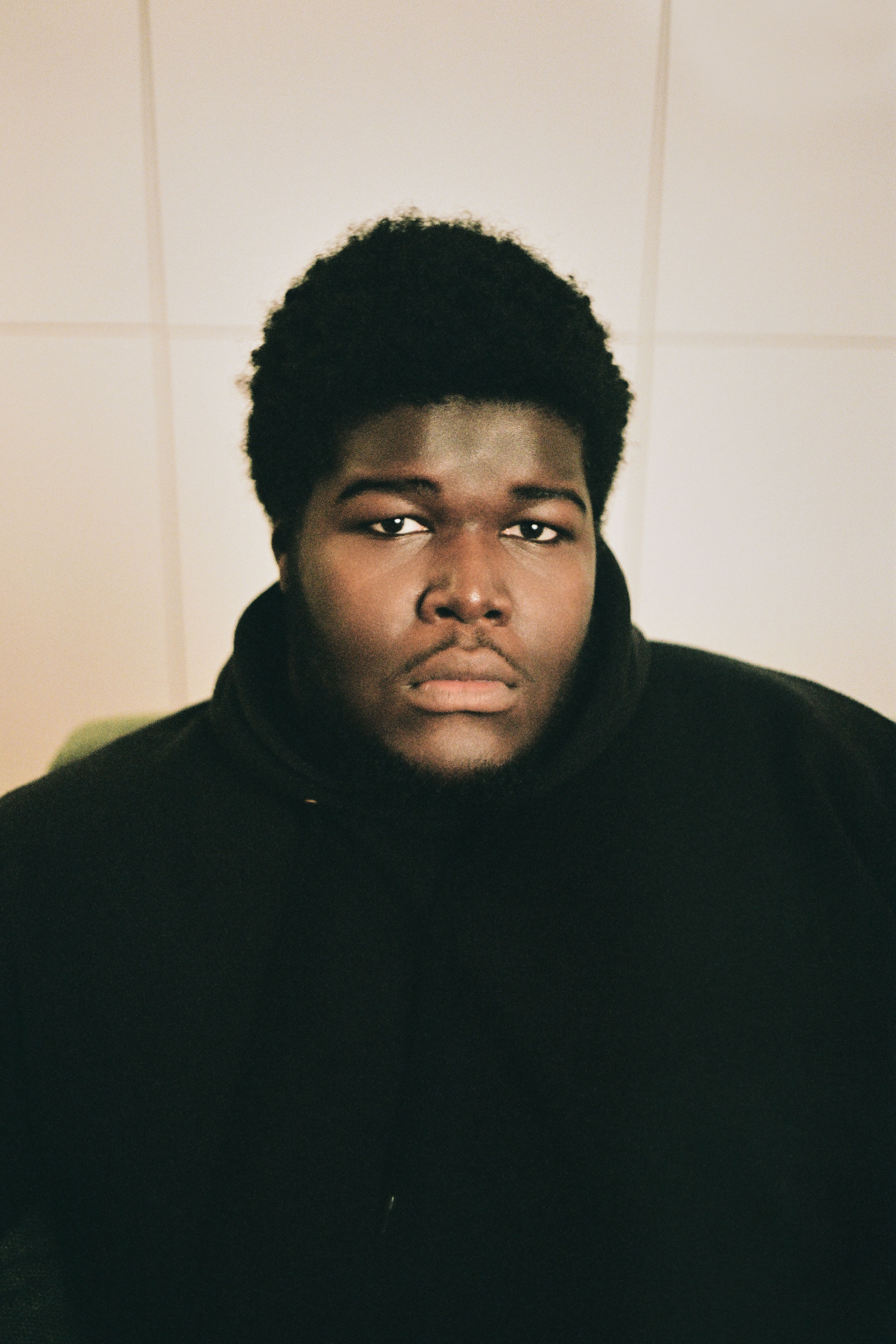 Portrait of Danish artist BUKURU wearing a black hoodie in a softly lit editorial setting.