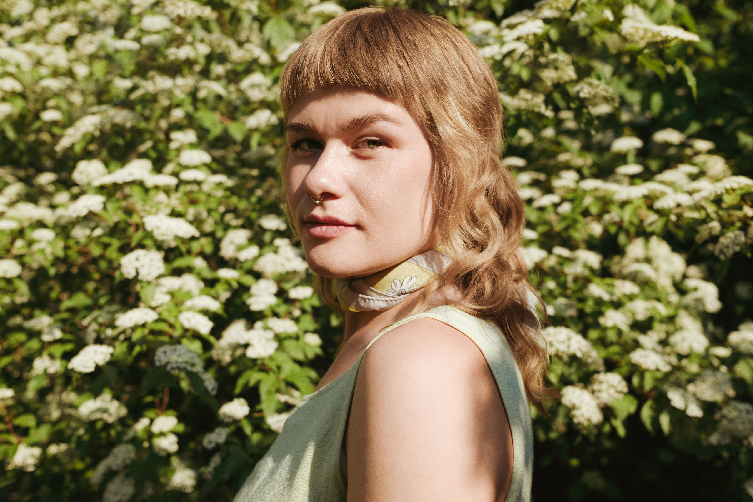Portrait of Danish artist Katinka Askehave standing among blooming white flowers in warm evening light.
