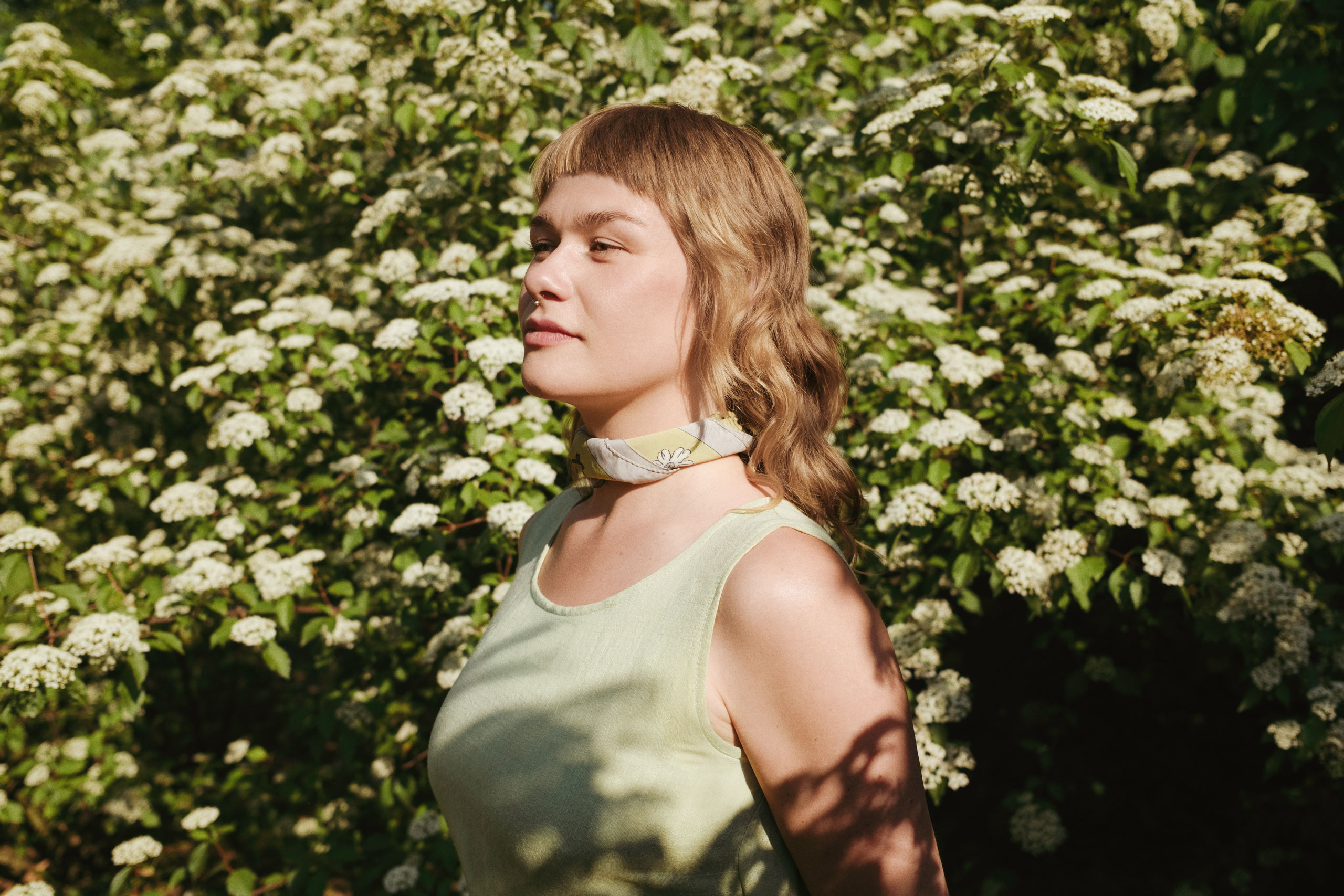 Side profile portrait of Danish artist Katinka Askehave surrounded by blooming white flowers in natural sunlight.