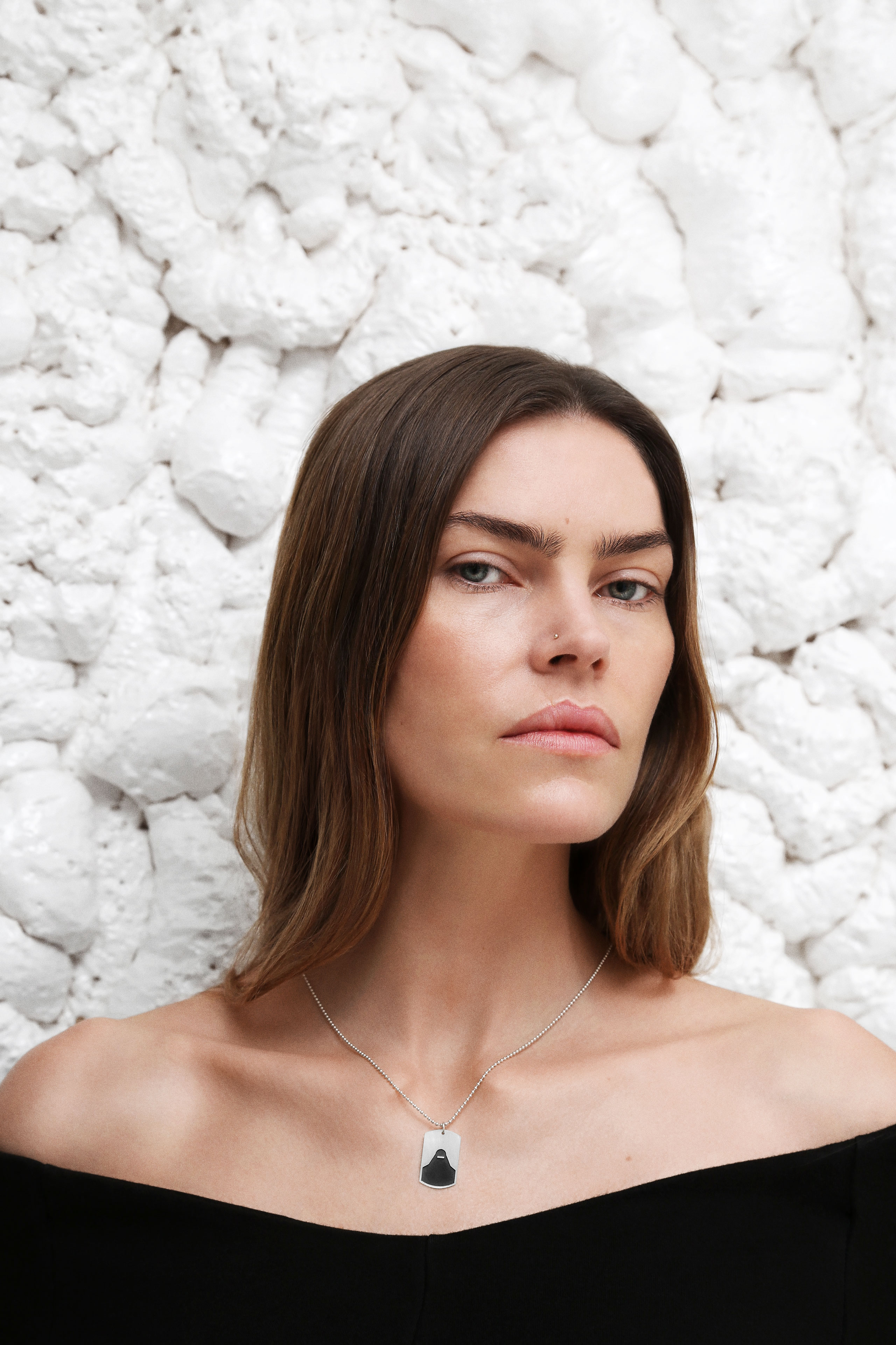 Fashion portrait of Lykke May wearing a silver pendant necklace from Persuede against a textured white stone background.