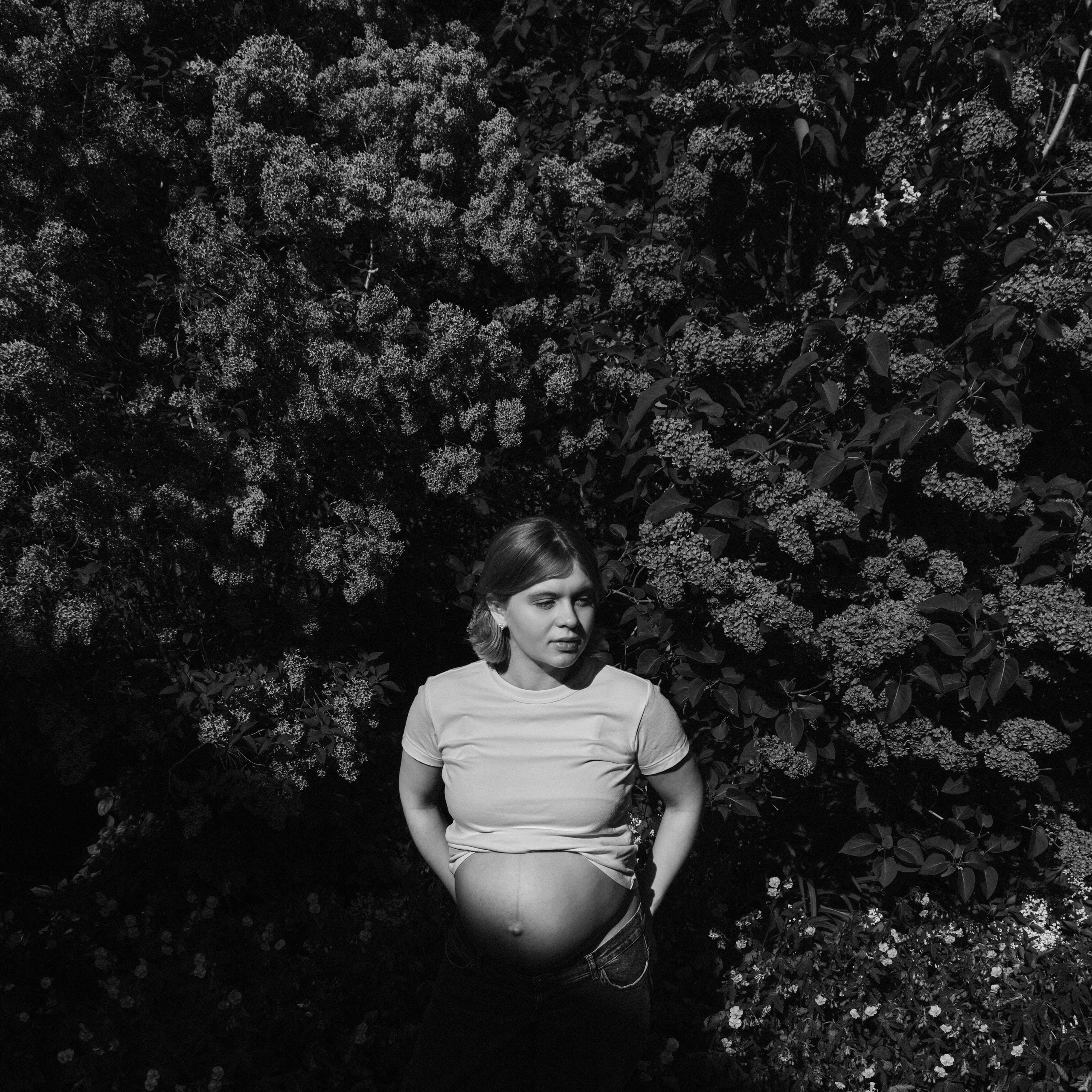     Black and white maternity portrait of Jana Katrín surrounded by flowering bushes in a Copenhagen garden.