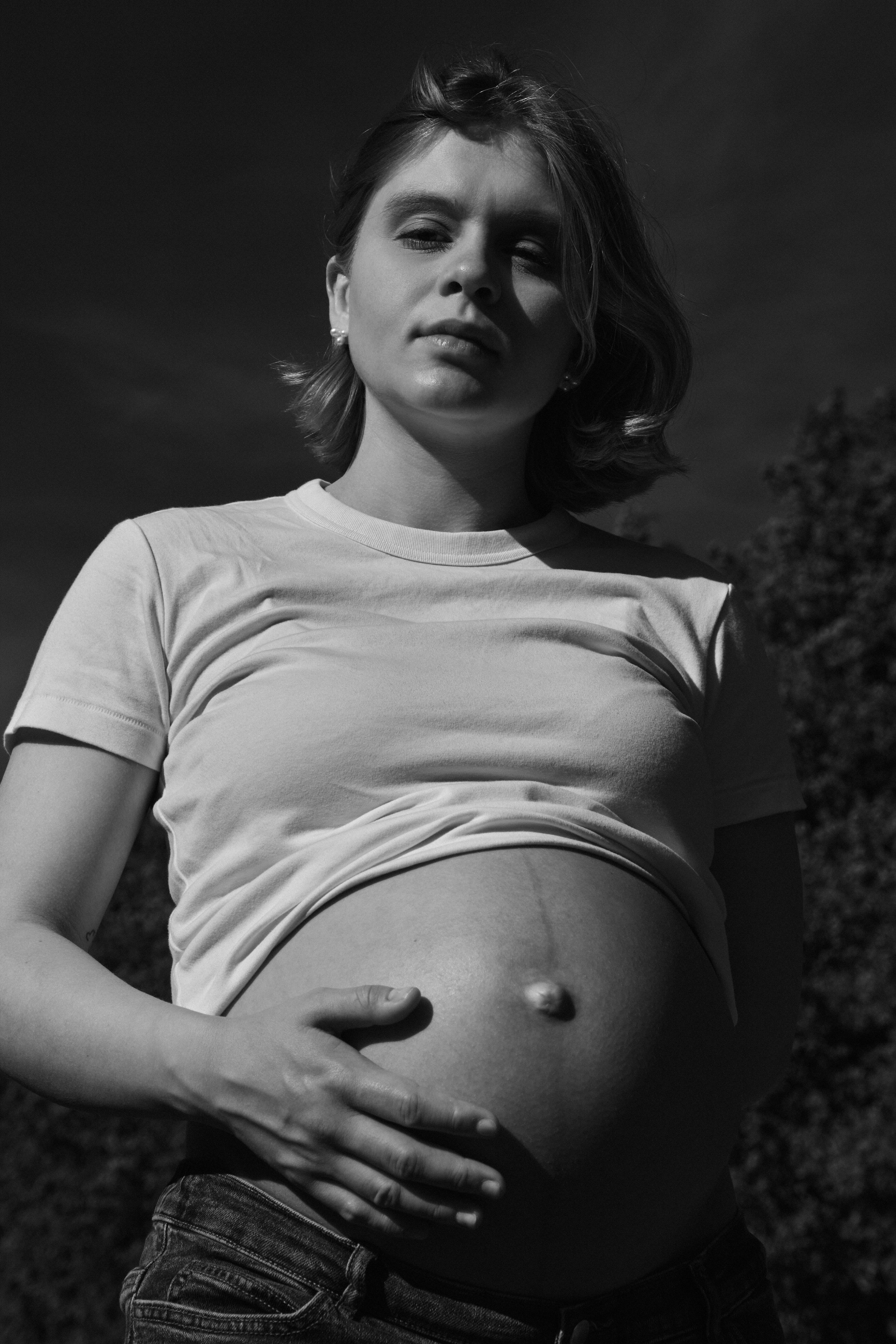     Black and white low-angle maternity portrait of Jana Katrín outdoors, photographed in dramatic sunlight.