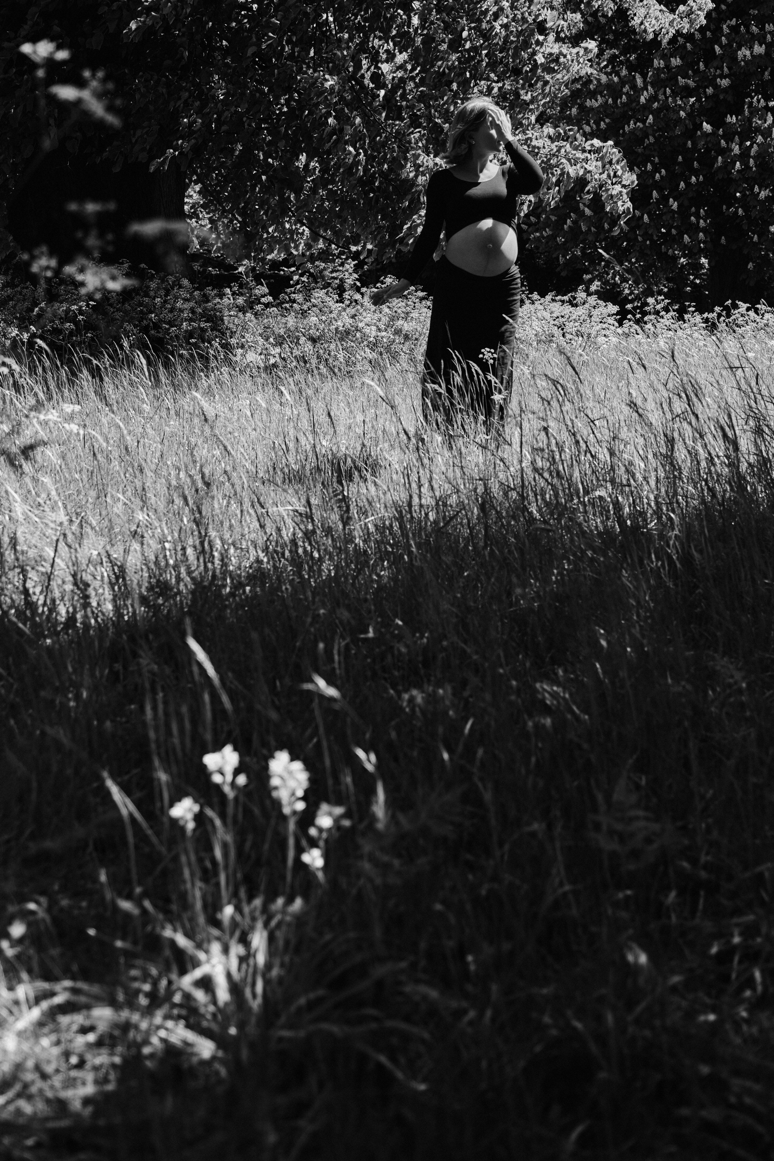     Black and white maternity photograph of Jana Katrín standing in tall grass and wildflowers in Copenhagen.