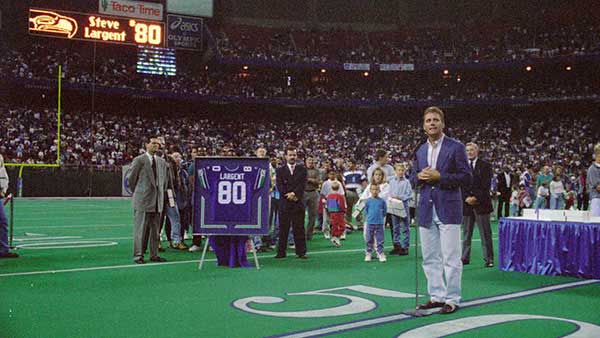 Steve Largent posing in front of his jersey at his retirement ceremony
