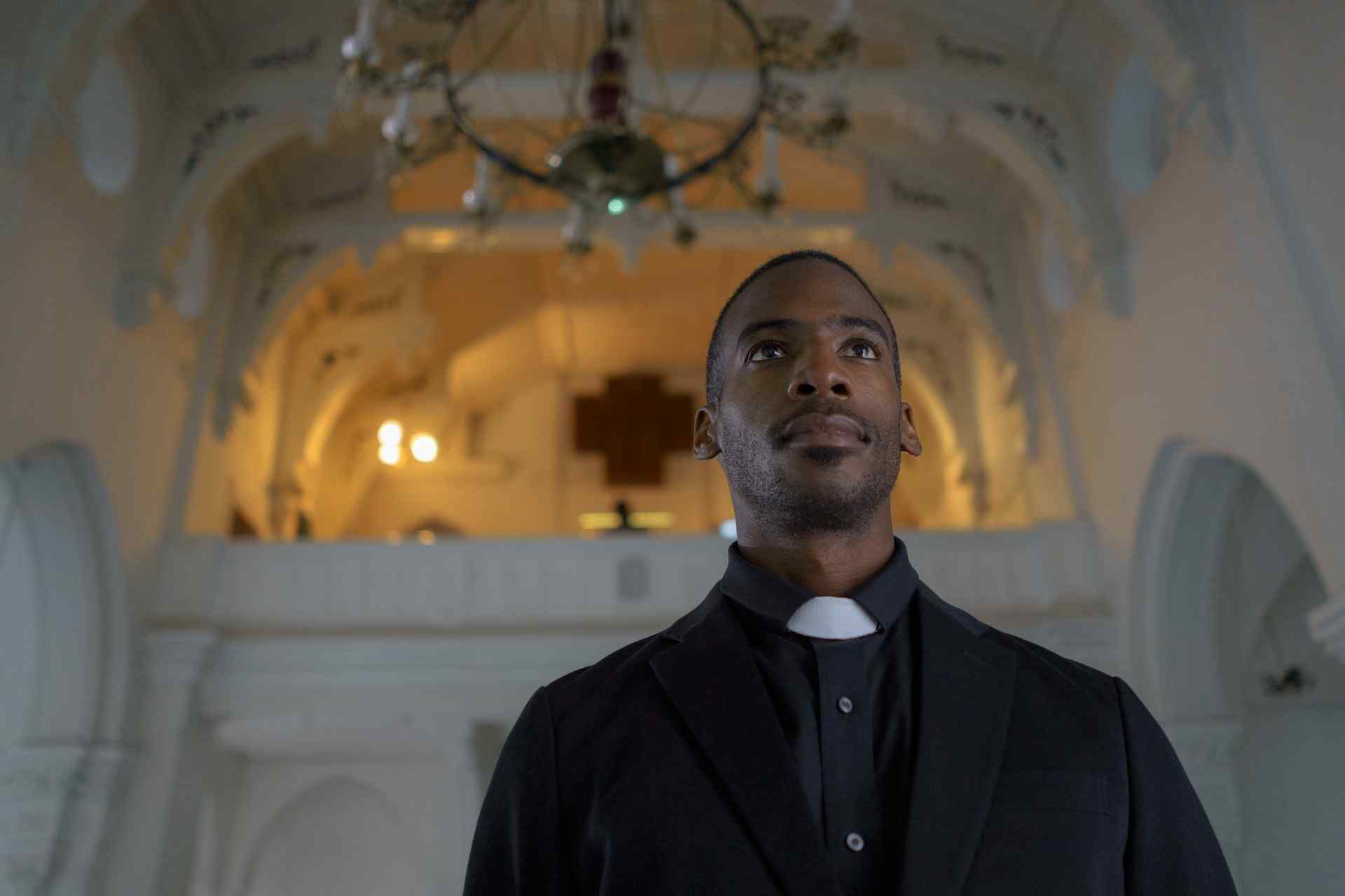 A man dressed in a black suit standing inside a church