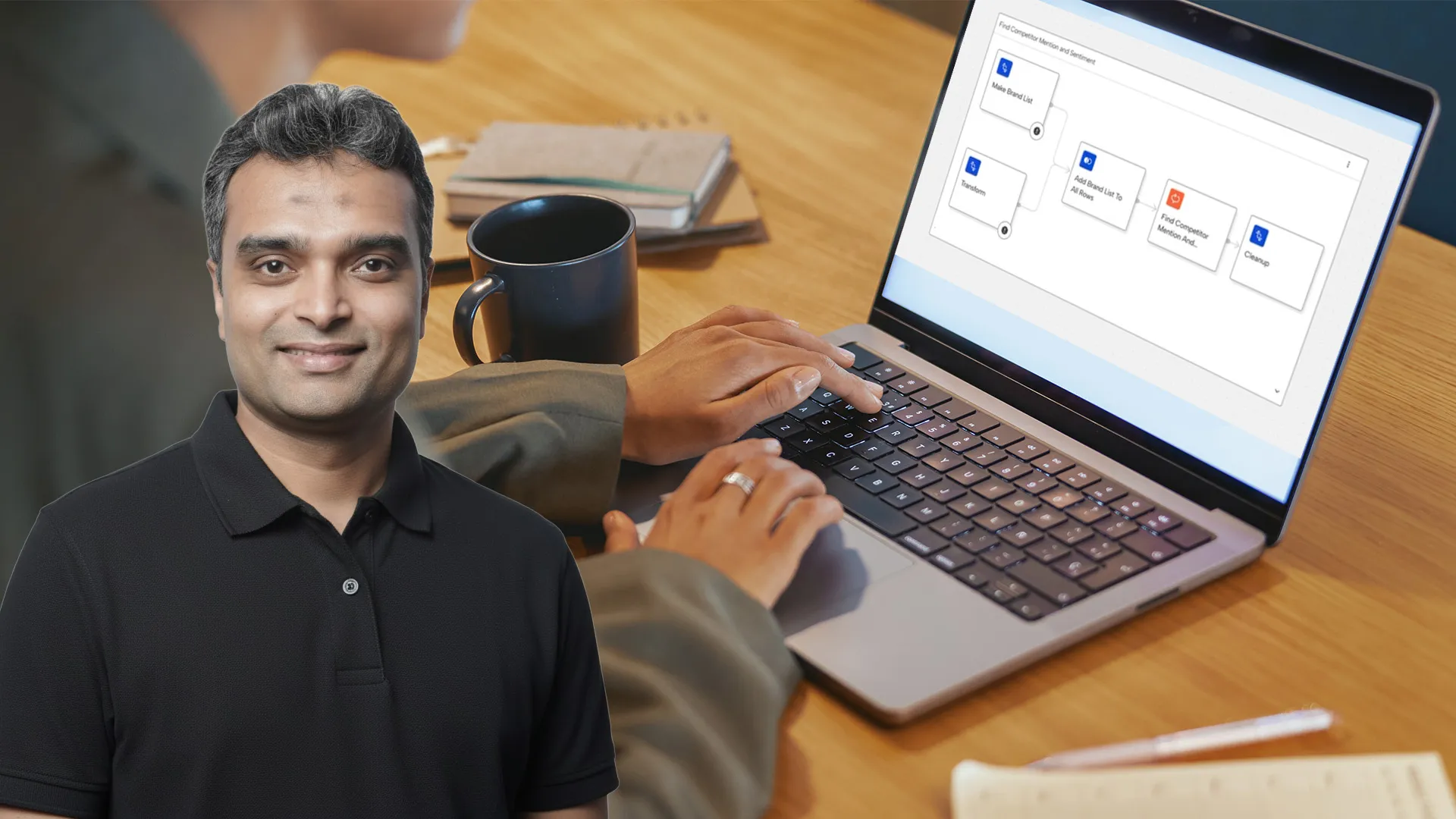 Man smiling in black polo shirt in front of laptop showing a workflow diagram on the screen.