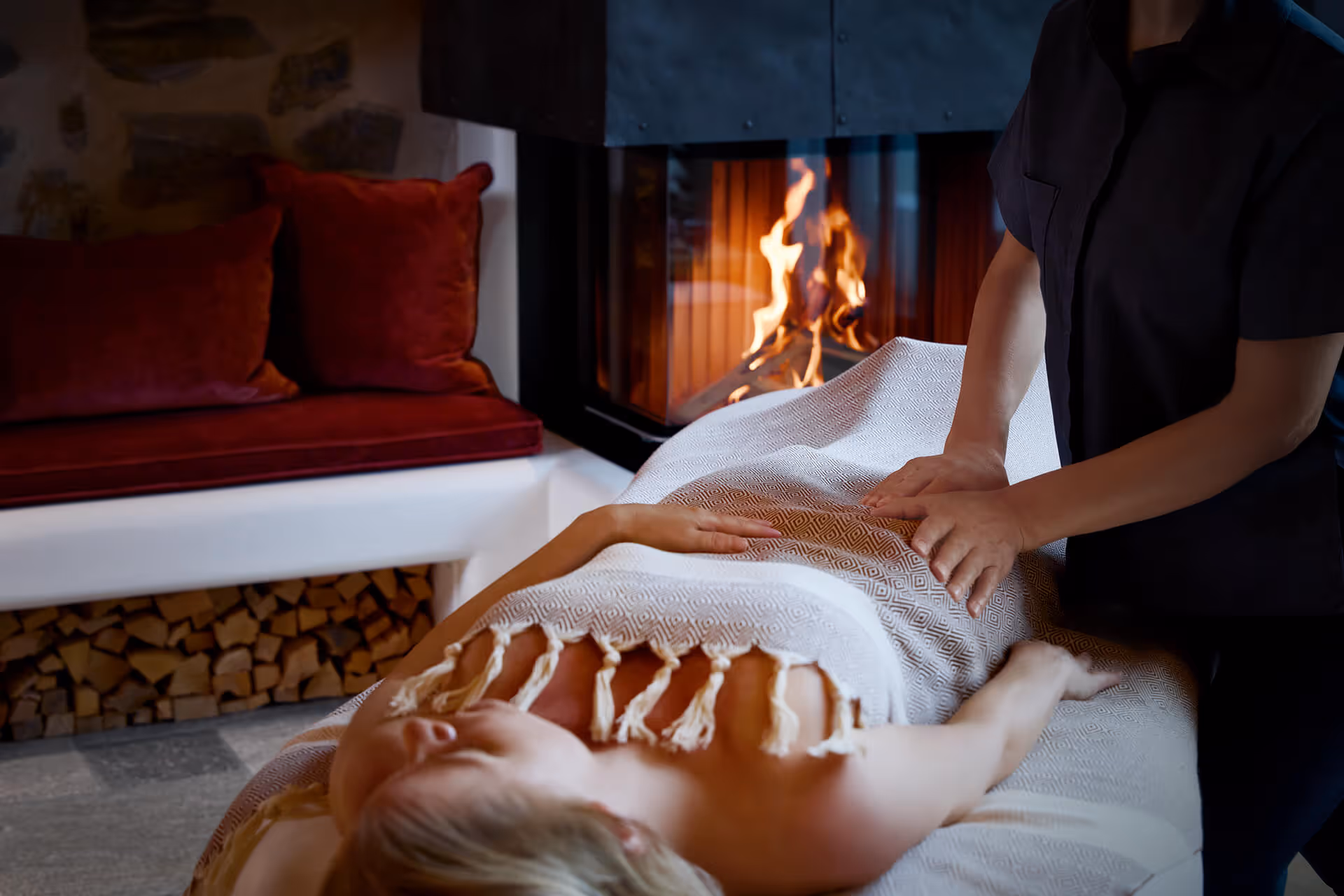 Eine Frau erhält eine Massage auf einer Massageliege vor einem gemütlichen Kamin.